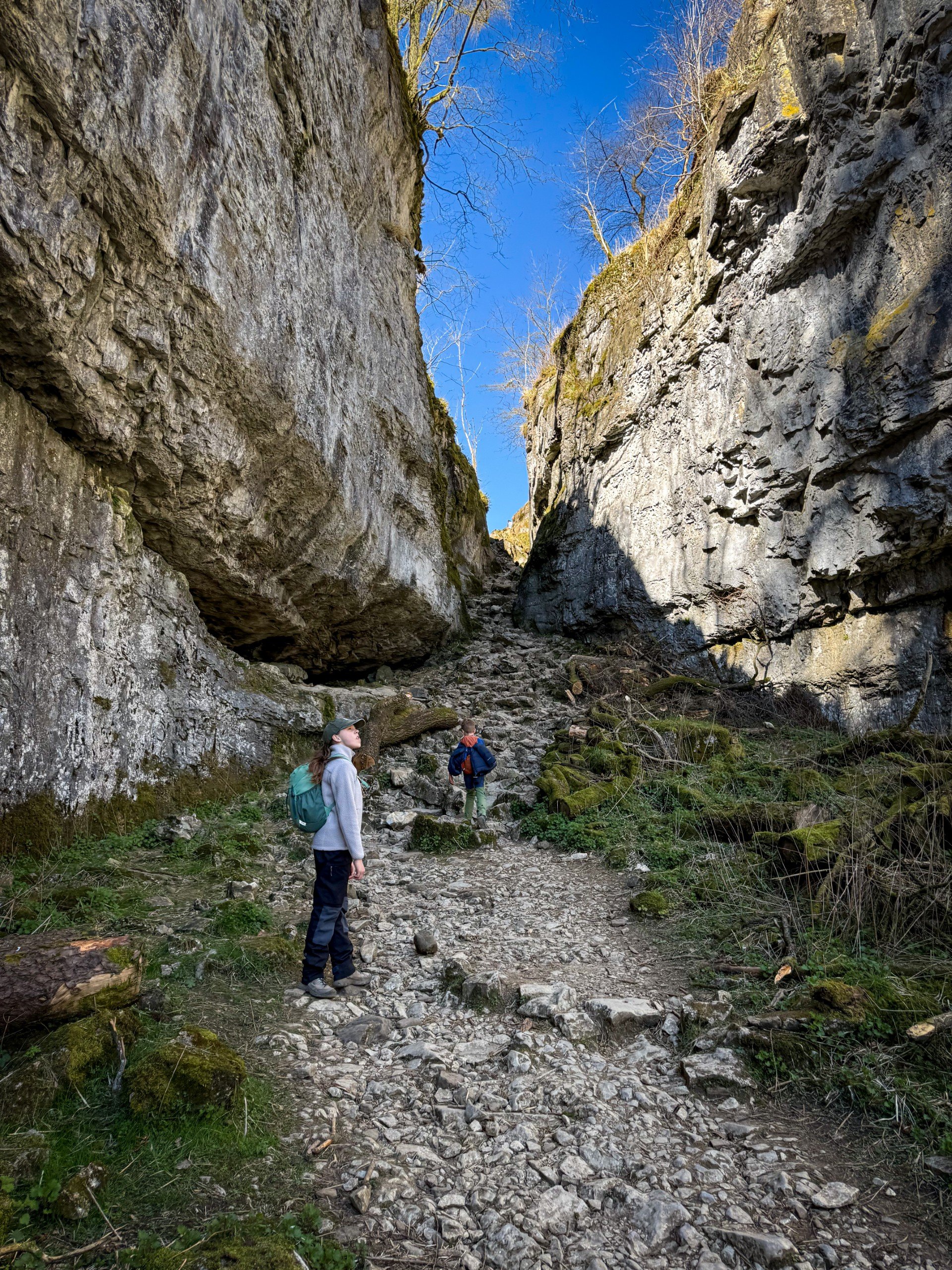 Children looking up at steep rocky cliffs in trow gill with blue skies beyond