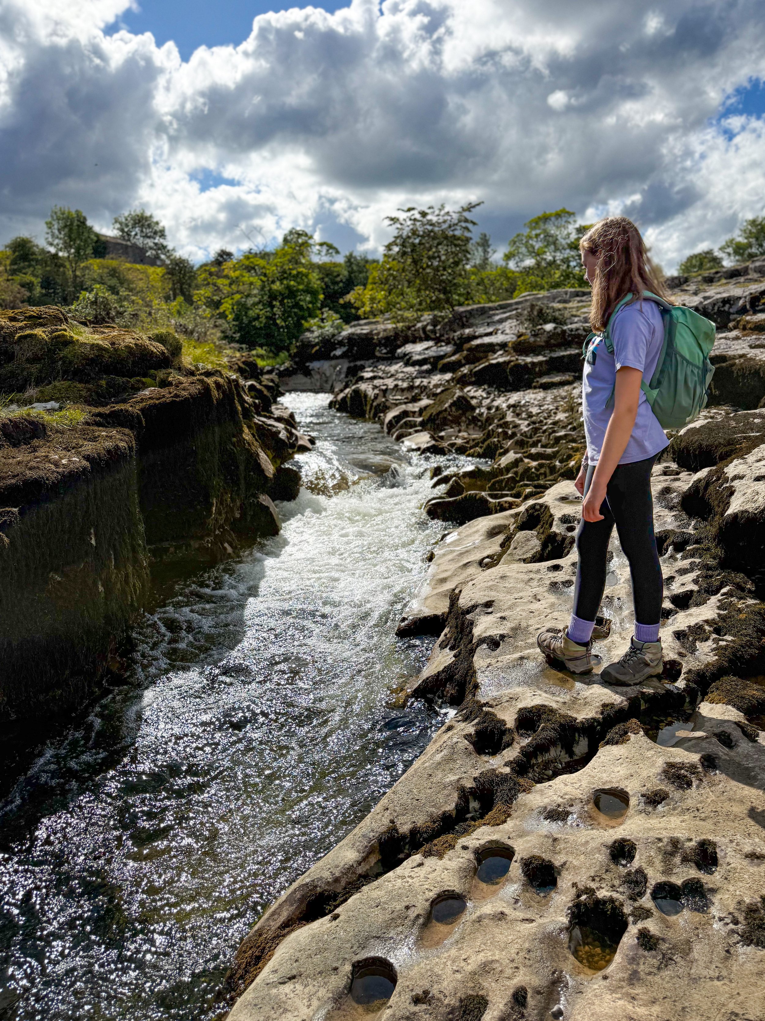 Child standing next to a rocky riverside with water bubbling through under blue skies
