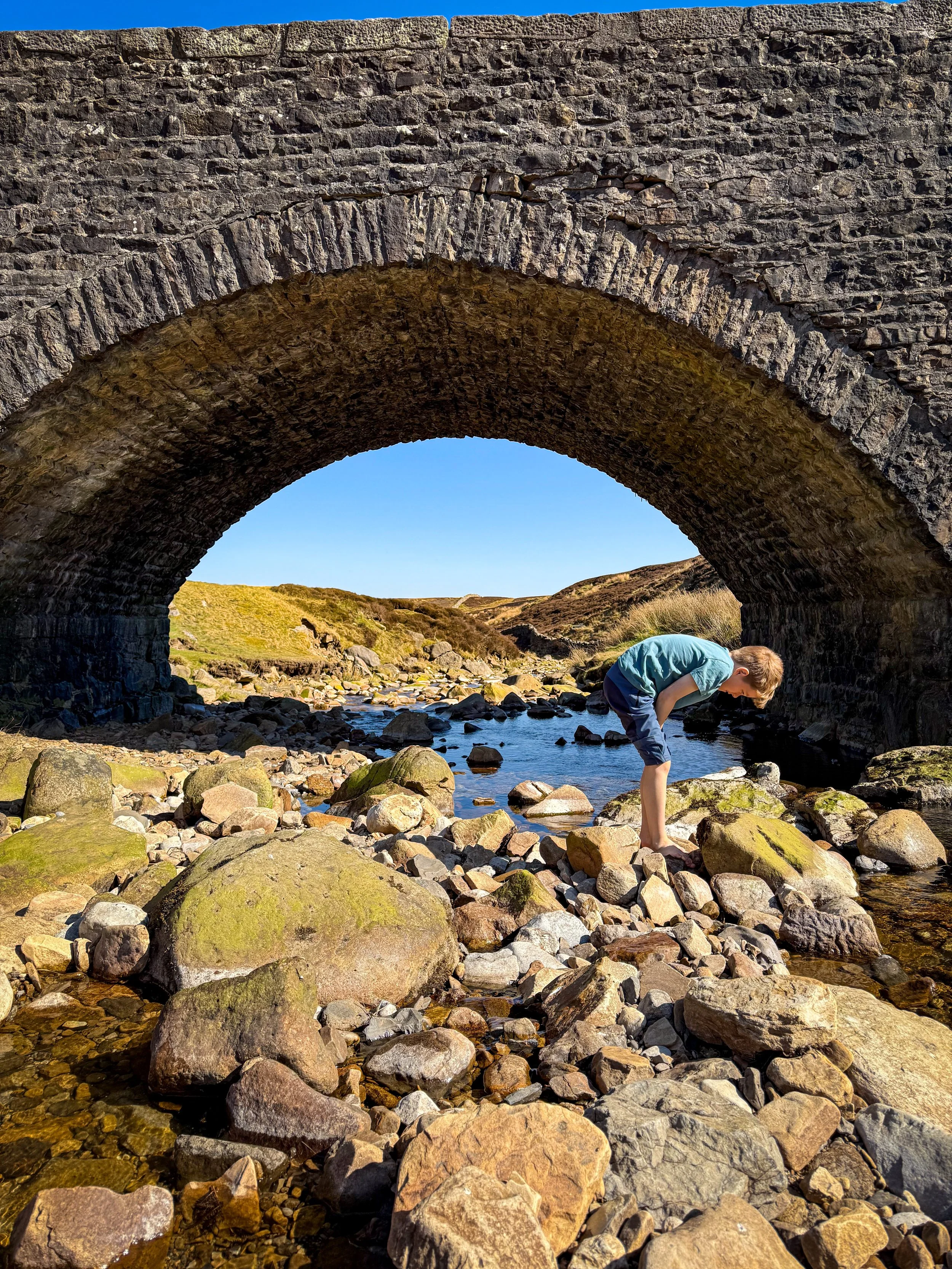 Child standing underneath a bridge with water