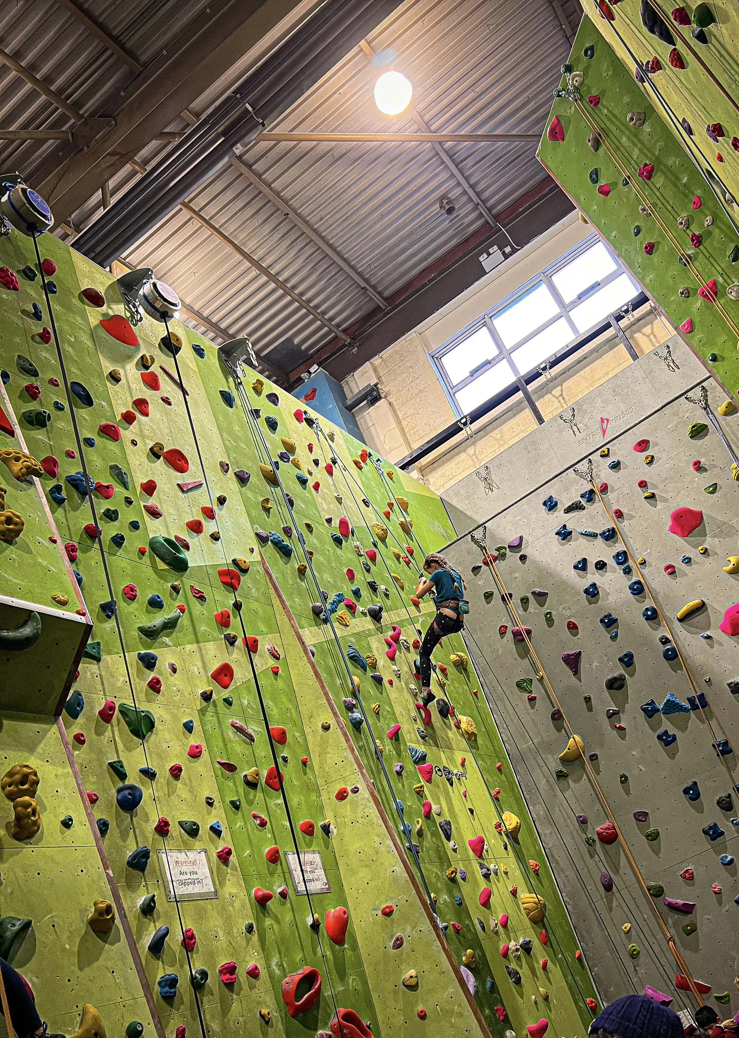 Child climbing up a large green indoor climbing wall