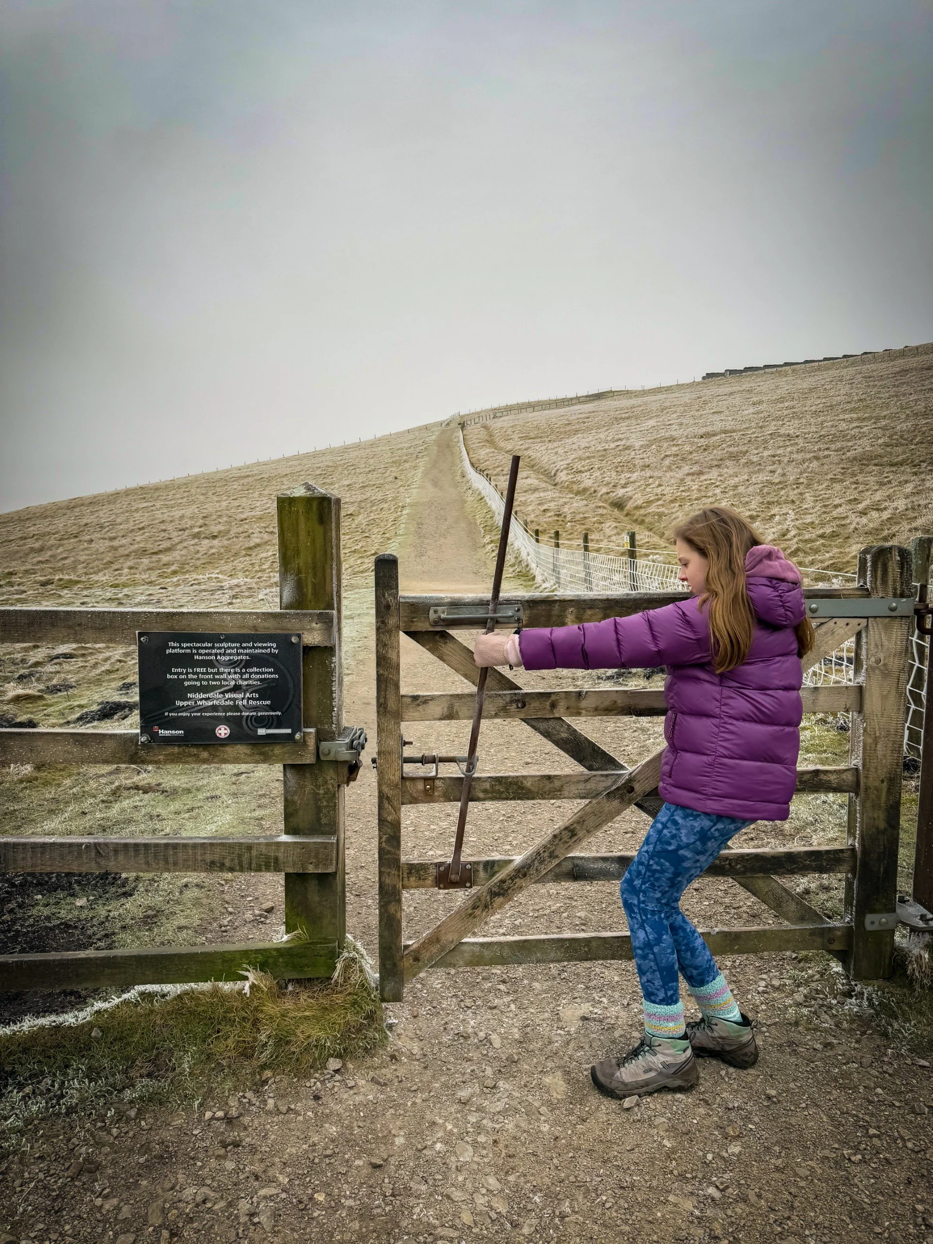 Child pulling lever on a gate in cold frosty conditions with rising path behind