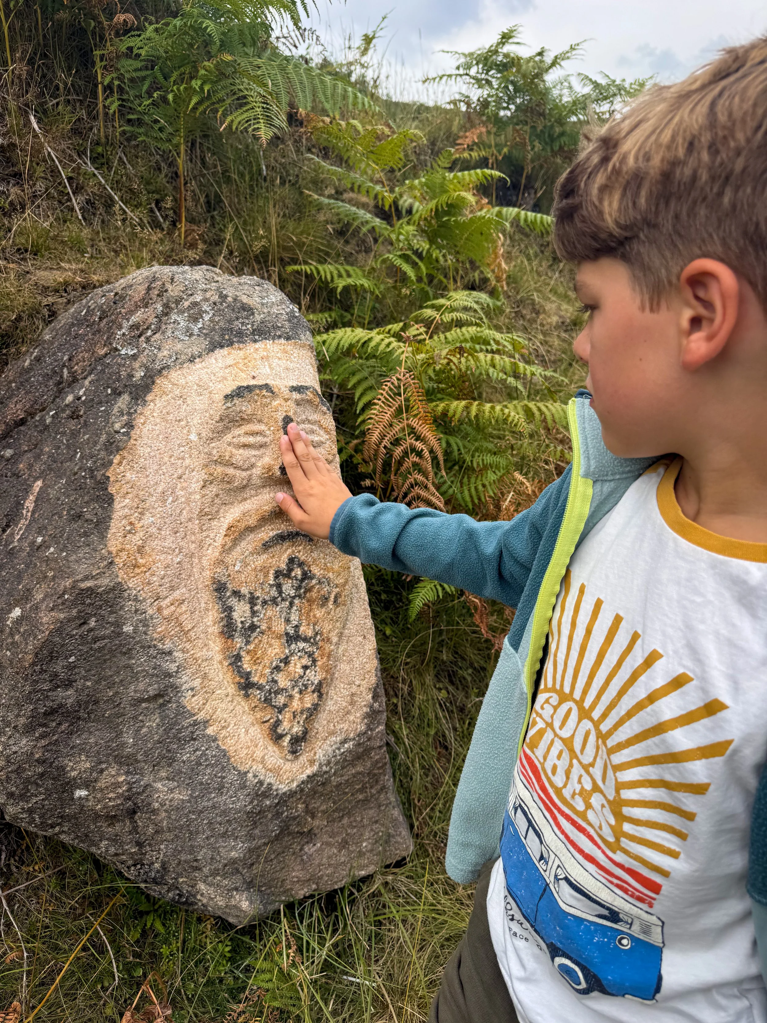 A child touching a stone carved face with ferns in the background