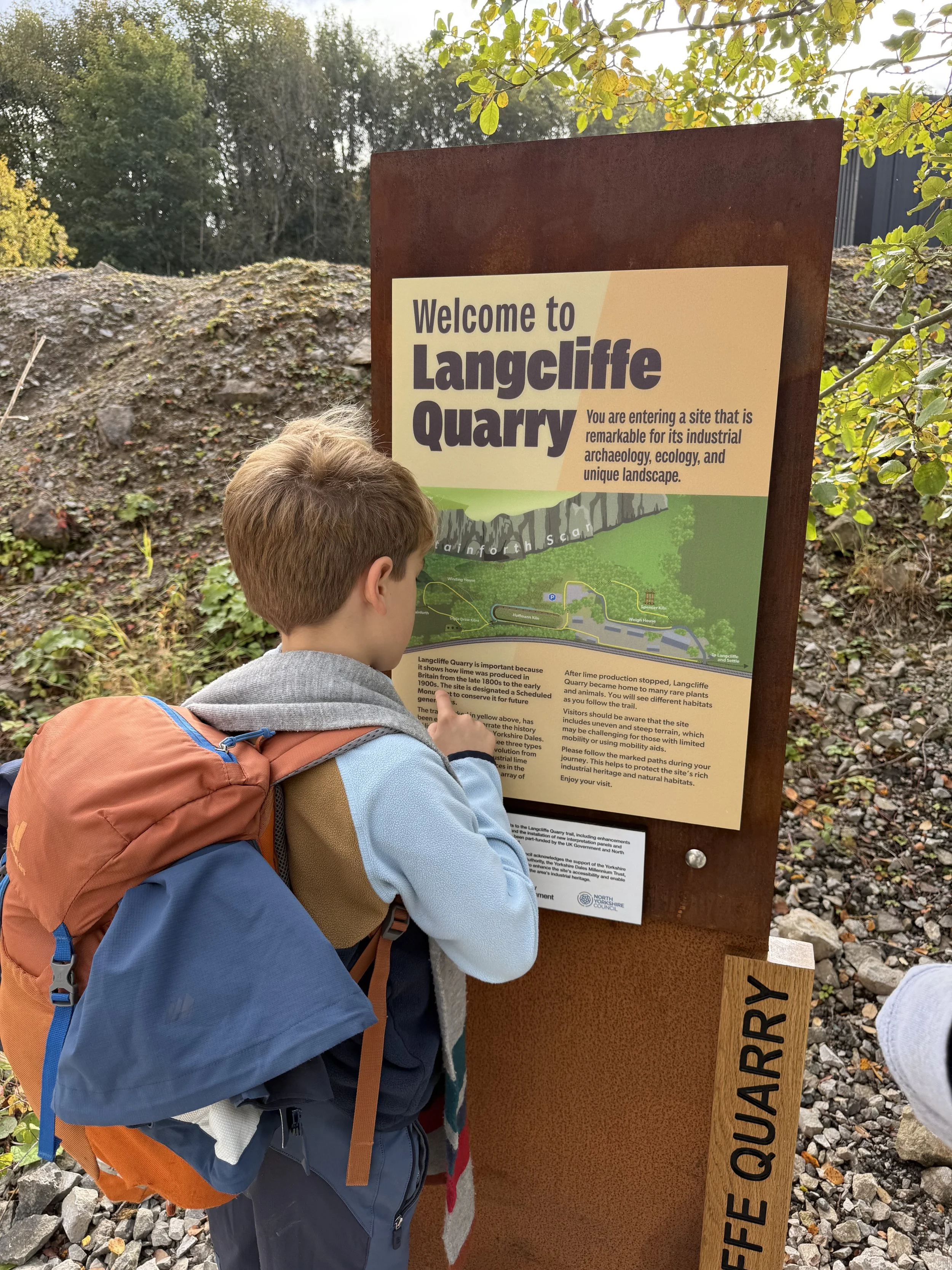 A child reading an information board entitled welcome to Langcliffe Quarry