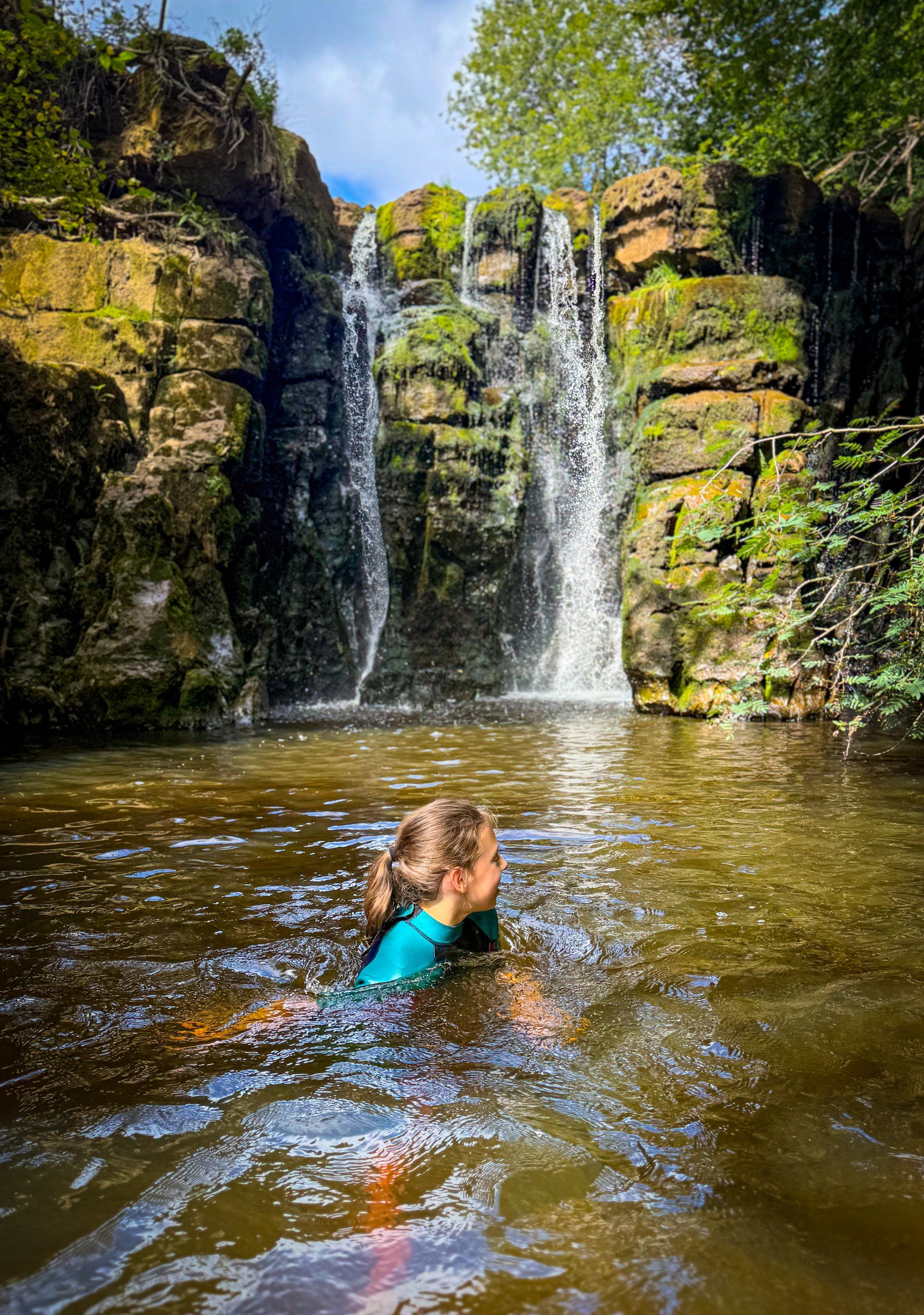Child swimming in a waterfall with a rocky cliff face