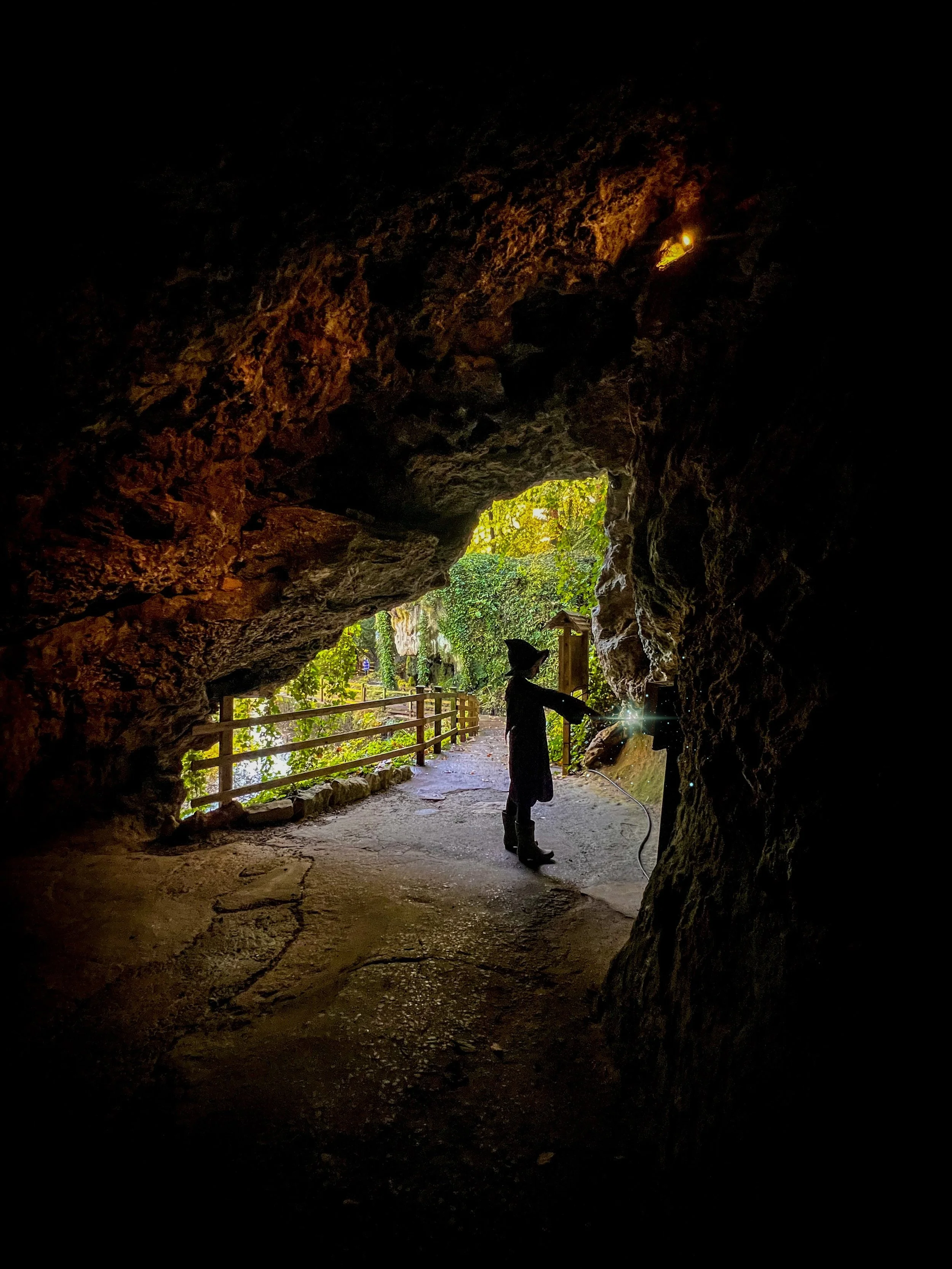 A child dressed as a witch with a magic wand in the mouth of a cave