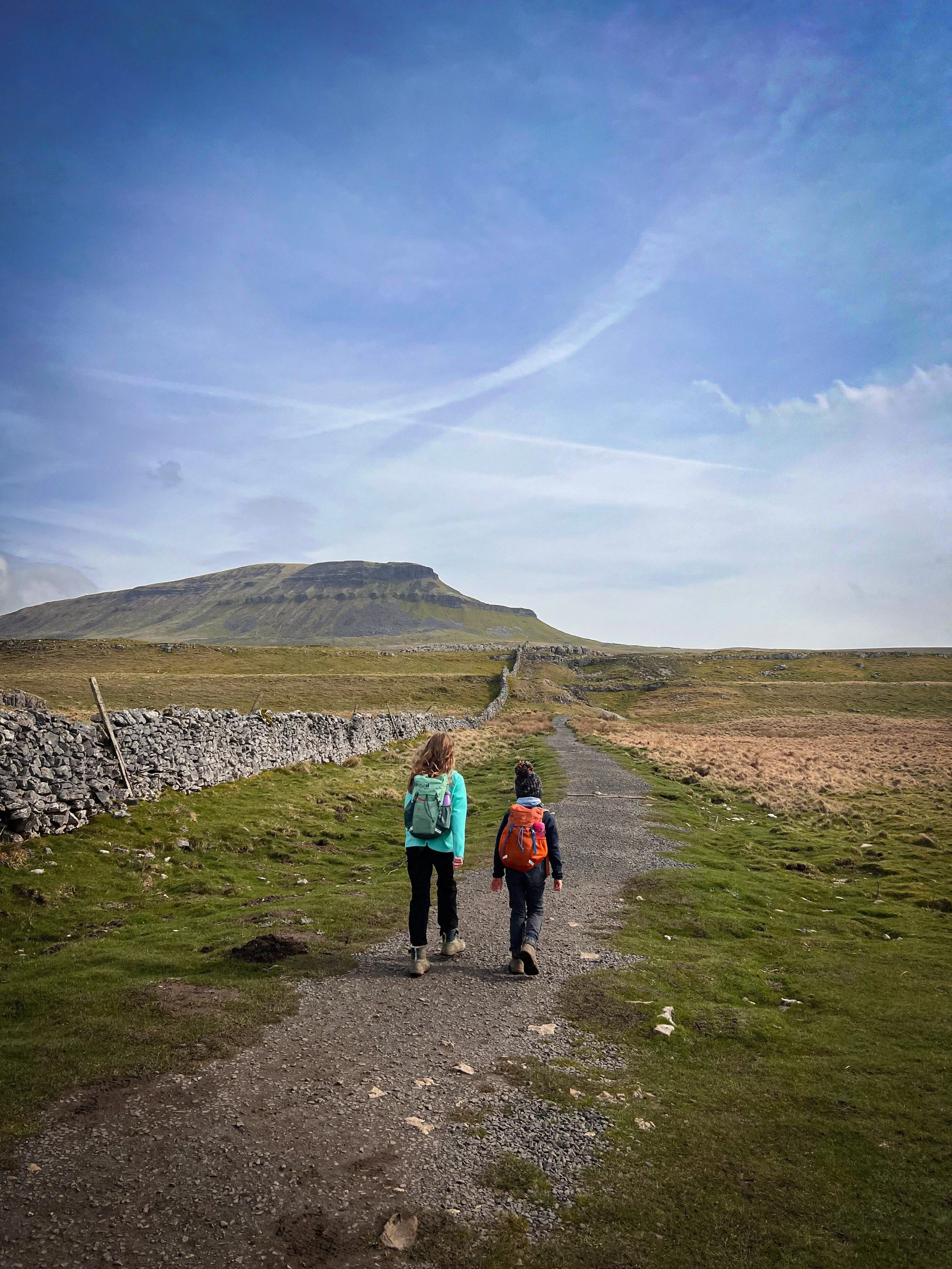 Two children walking towards Pen y ghent mountain under blue skies walking along a rocky dry stone wall