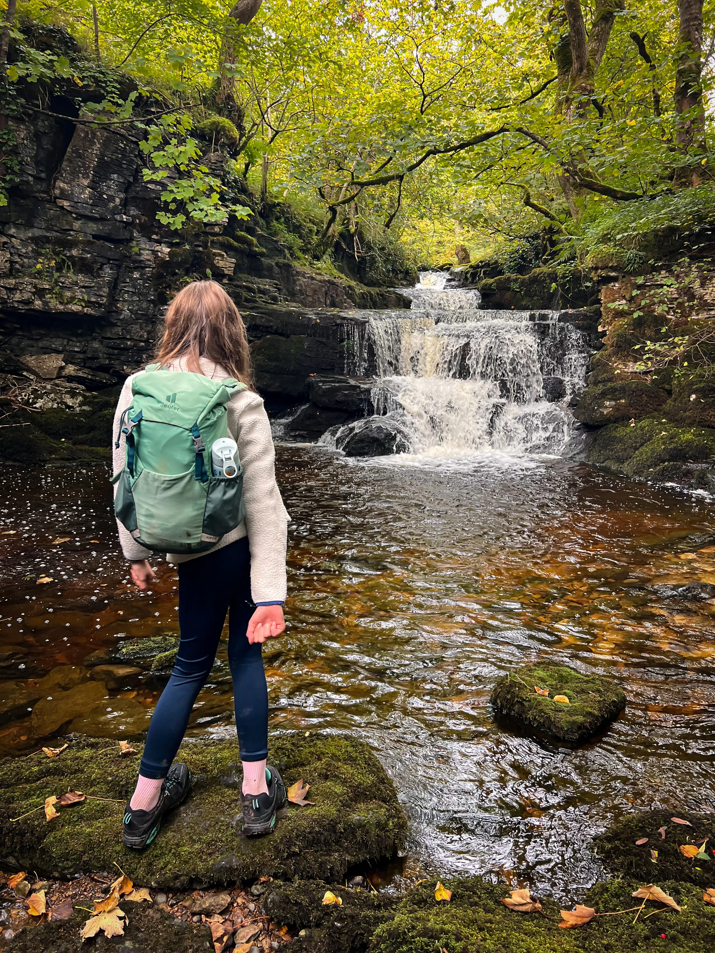 Child standing looking at a cascading waterfall in Autumn