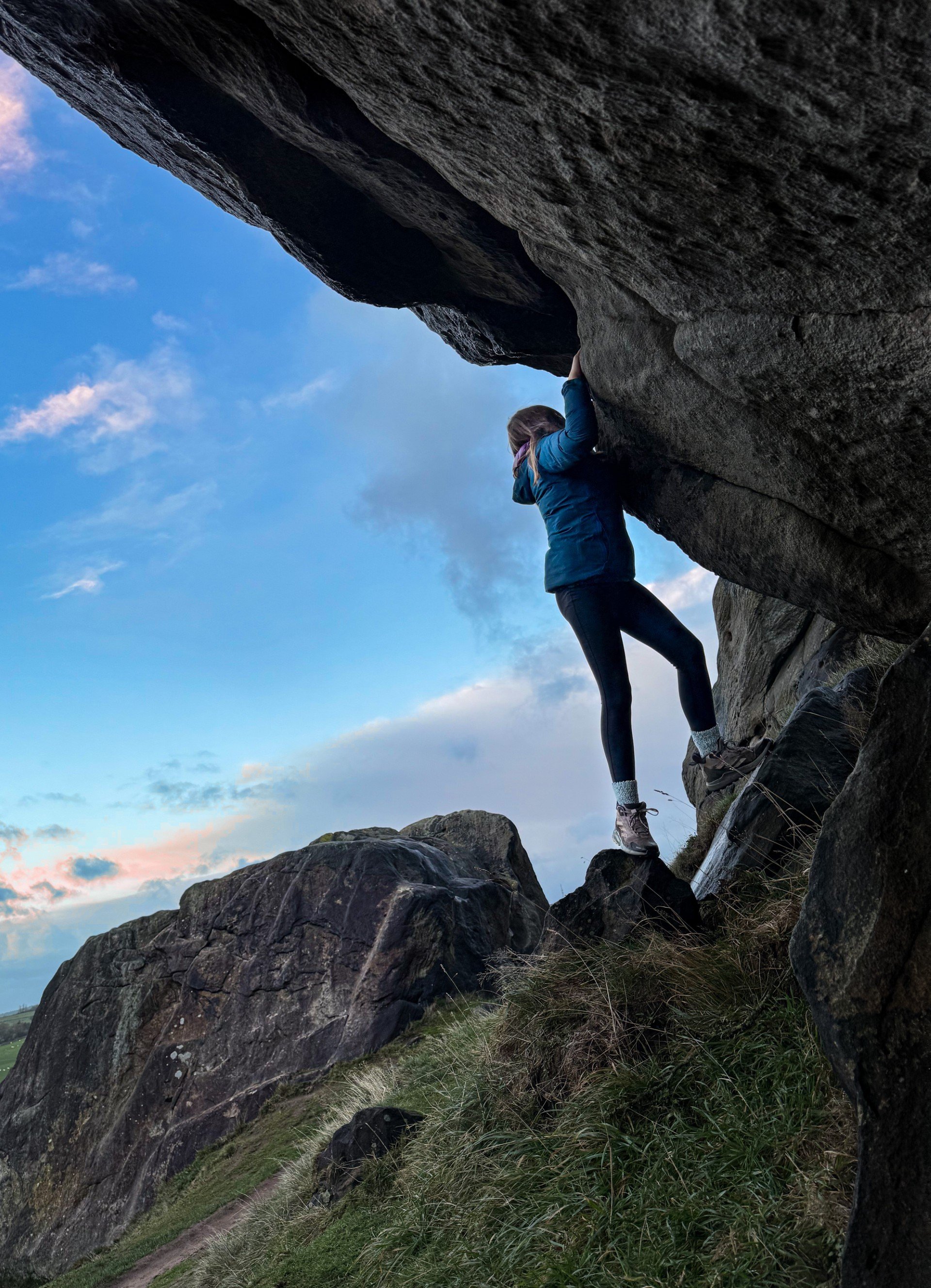 Child silhouetted against a sunset sky climbing on a large rock
