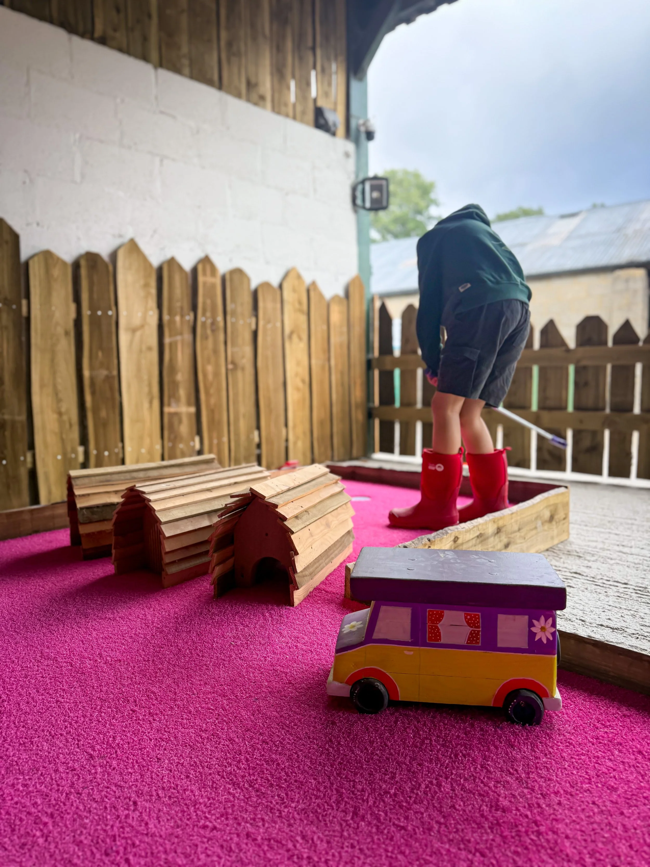Child playing crazy golf in a barn with a campervan themed hole