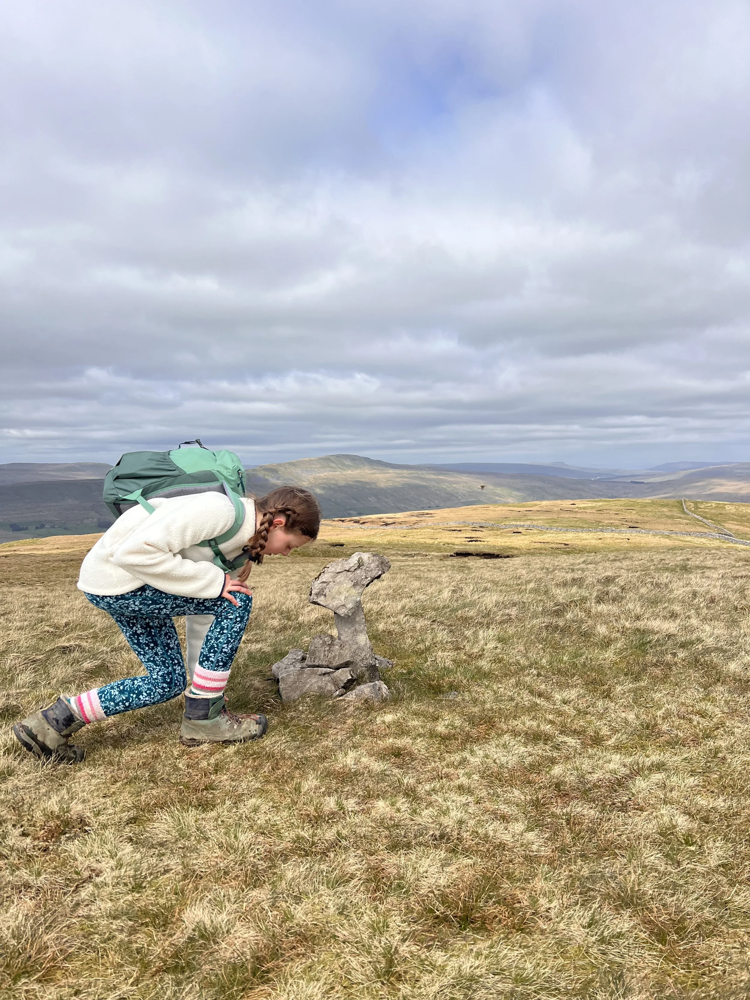 A child crouched next to a small pile of stones with mountains behind