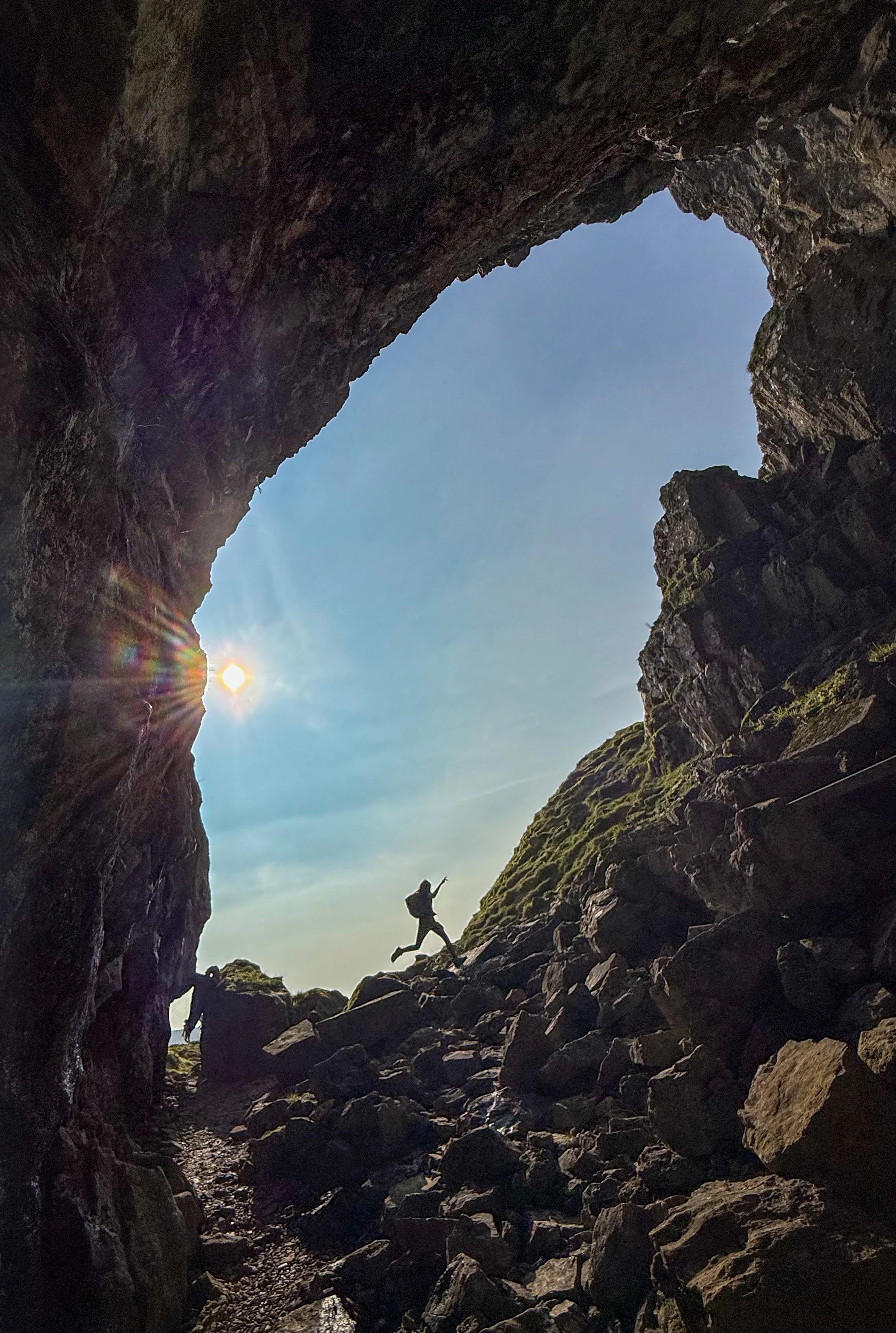 Child leaping in silhouette against a huge cave opening with sunbeams