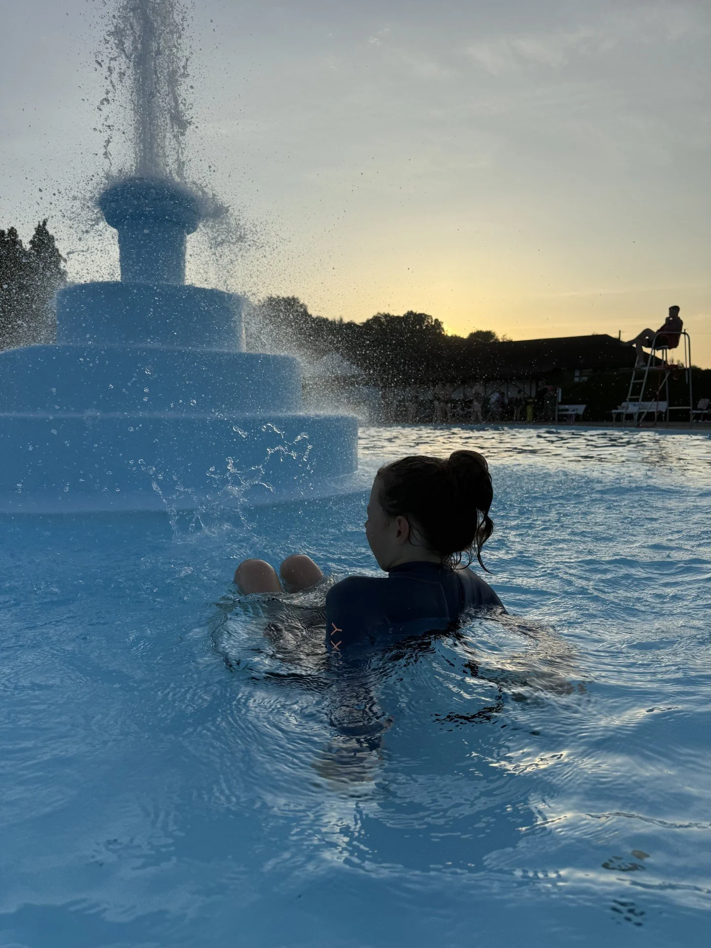 Child sitting in an outdoor swimming pool next to a fountain