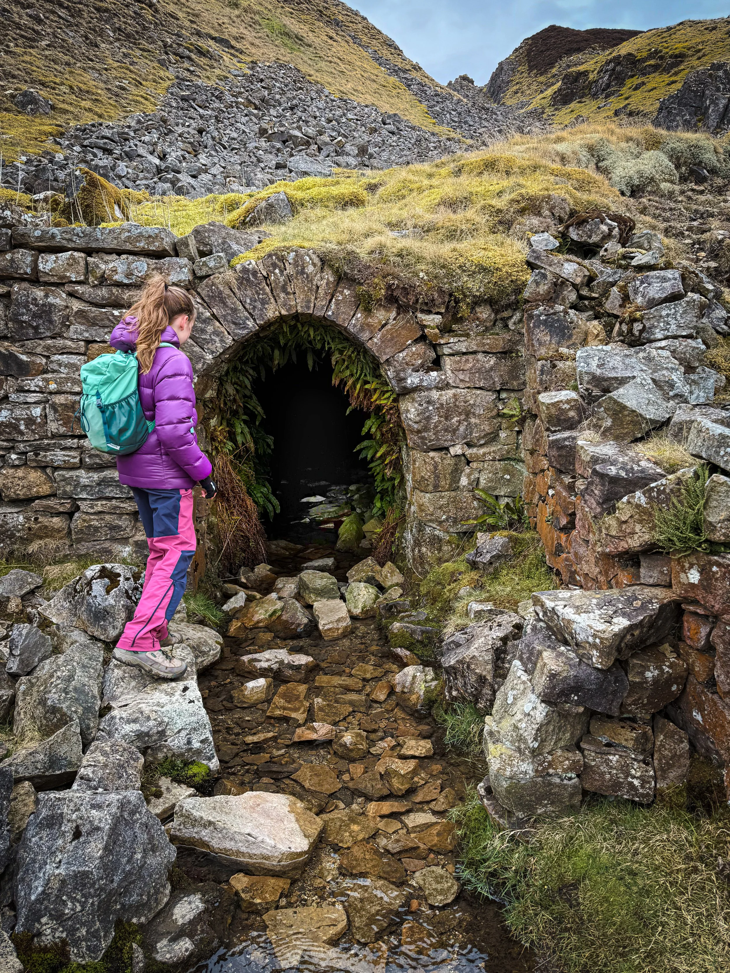 Child standing next to a mining tunnel wearing a purple coat