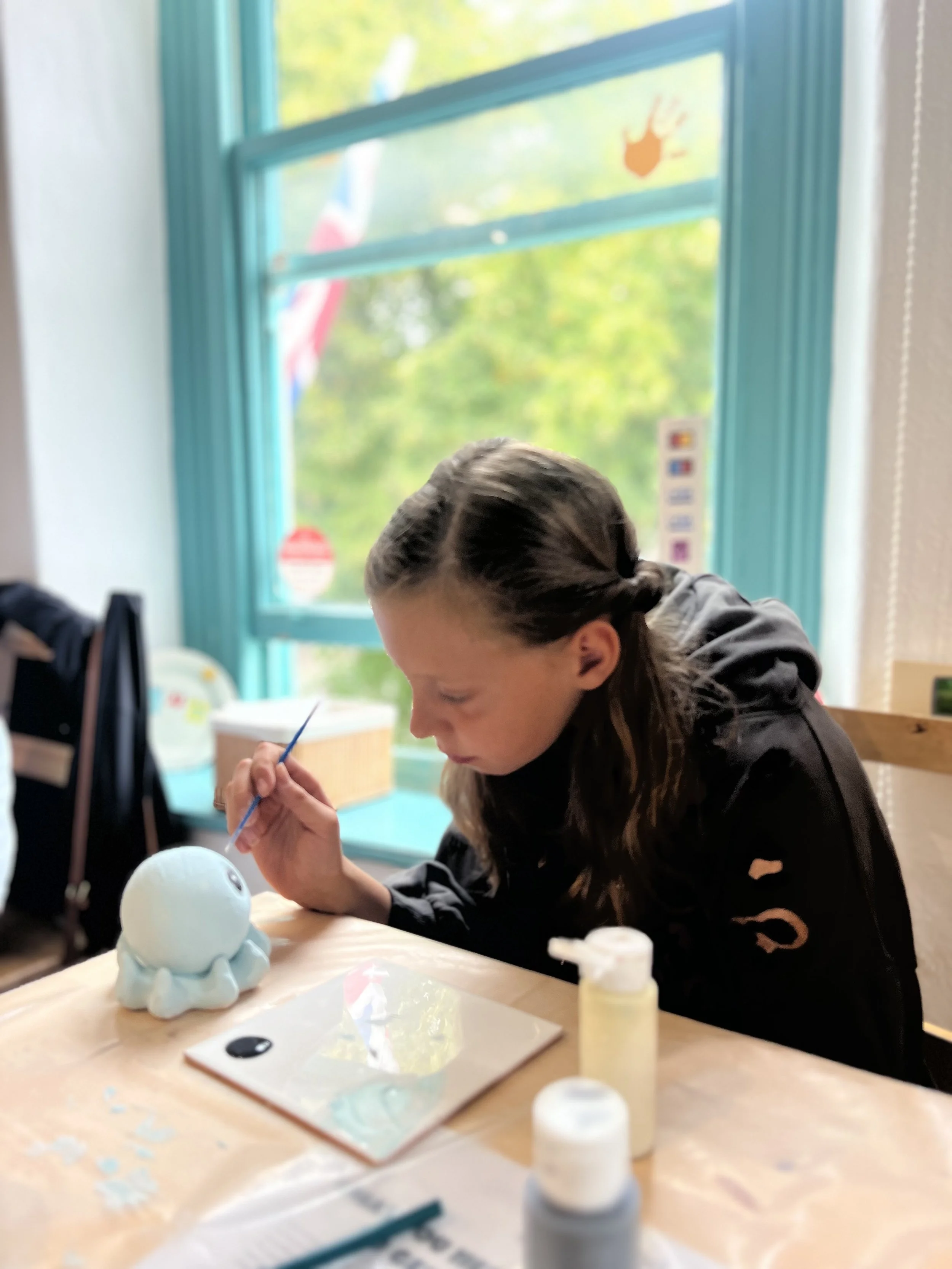 Child sitting painting a pottery octopus in front of a window