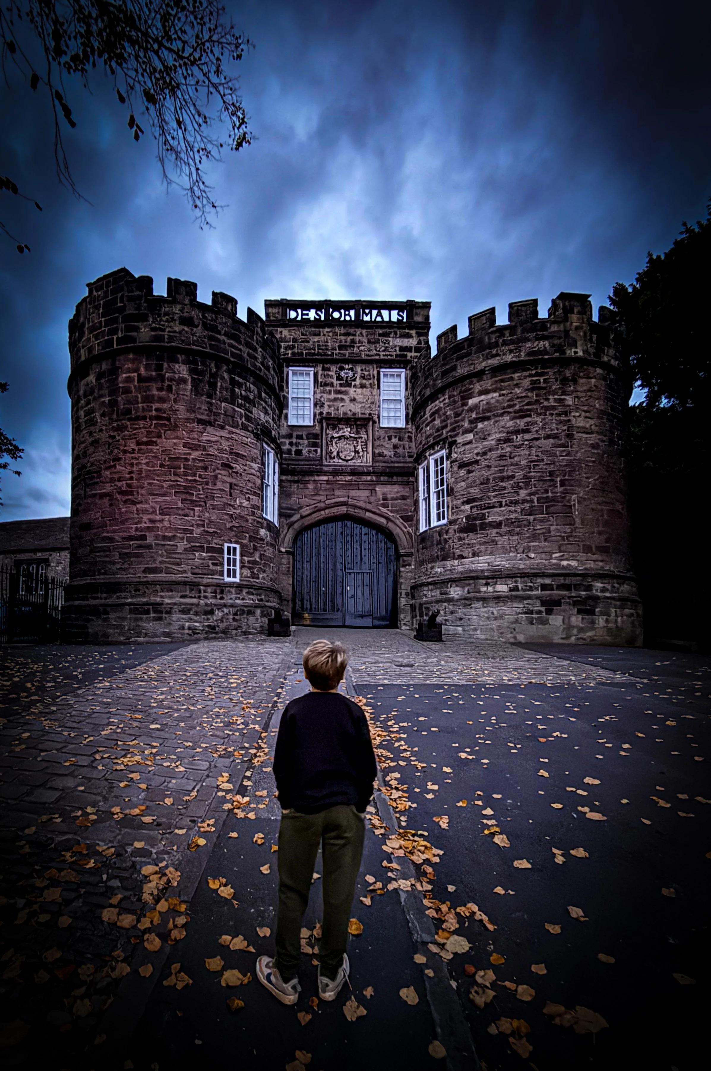 Child walking towards a castle with dark night skies and autumn leaves on cobbled street