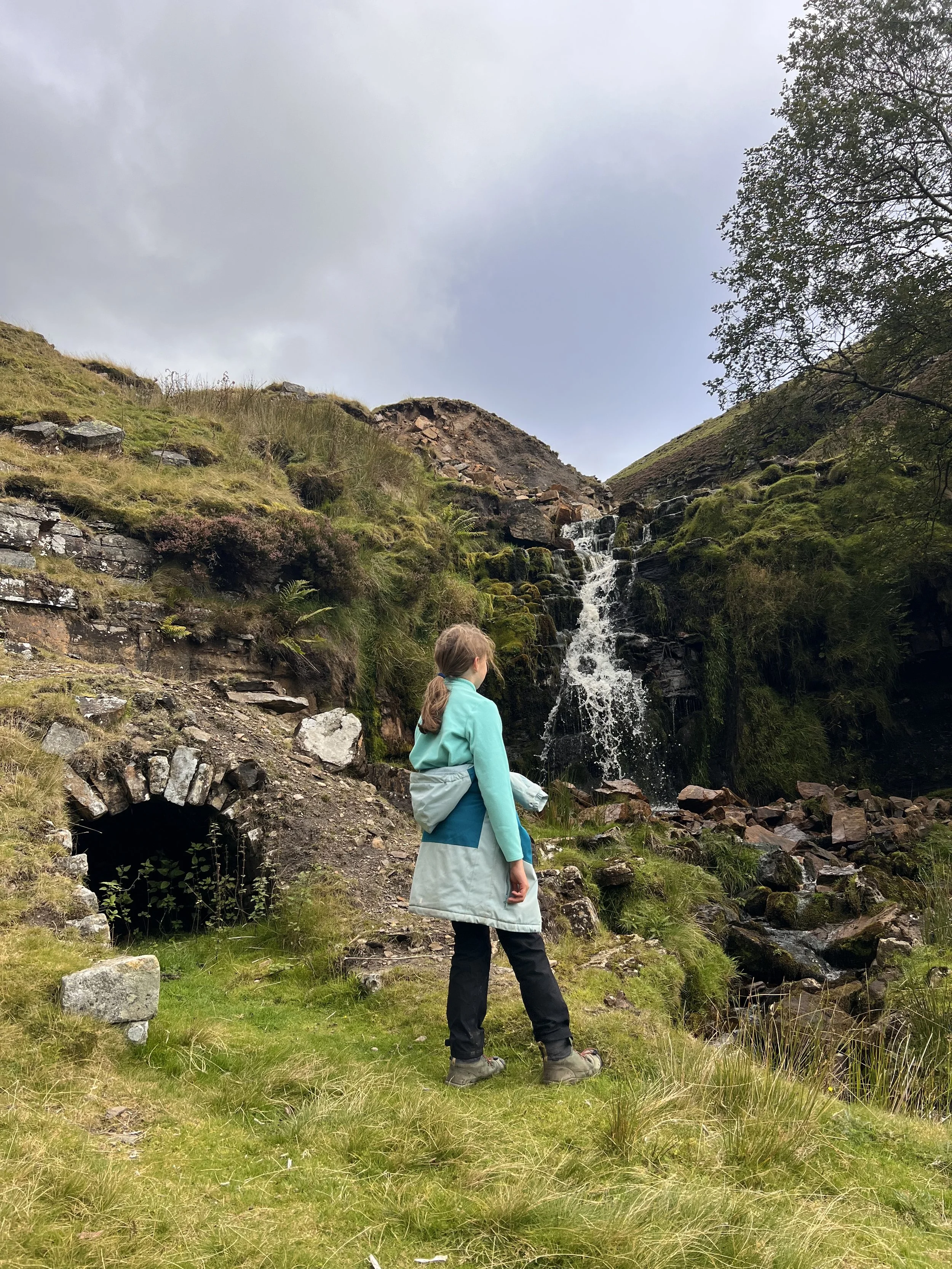 Child standing next to the ruins of a tunnel with a waterfall