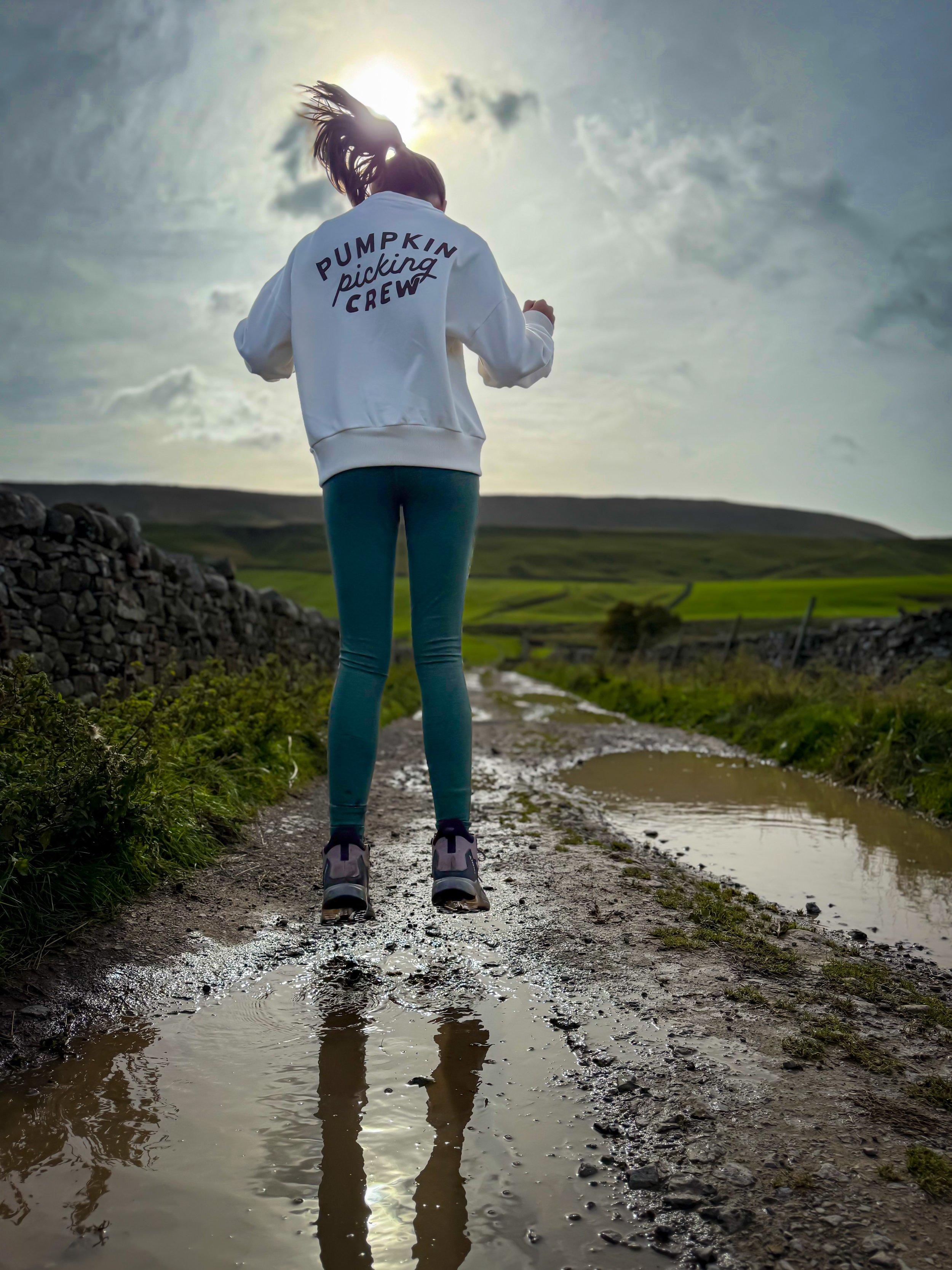 Child jumping in a puddle with a hill ahead under a sunny sky with a golden hue on a walled track