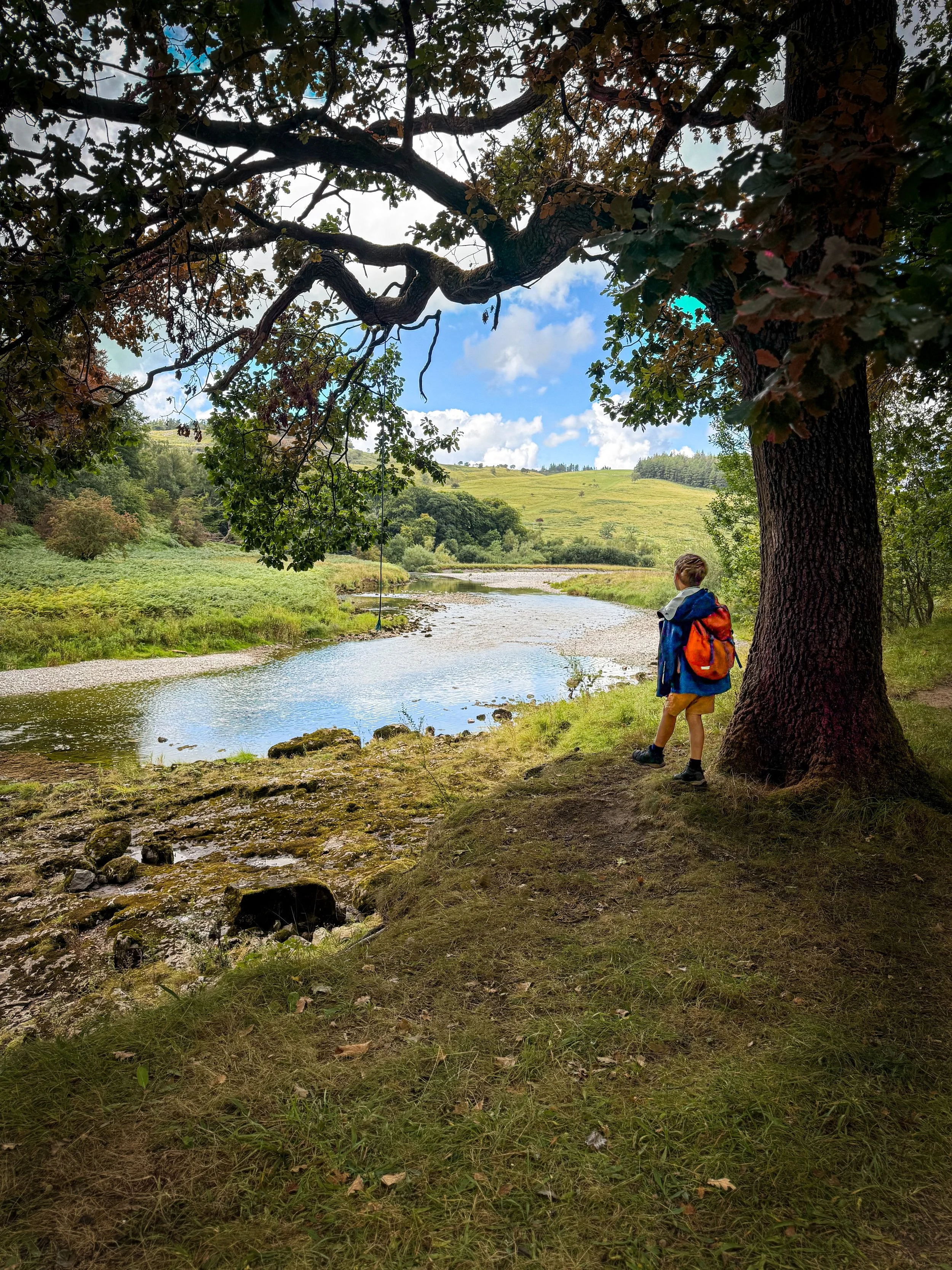 Child standing next to a tree with a river beyond
