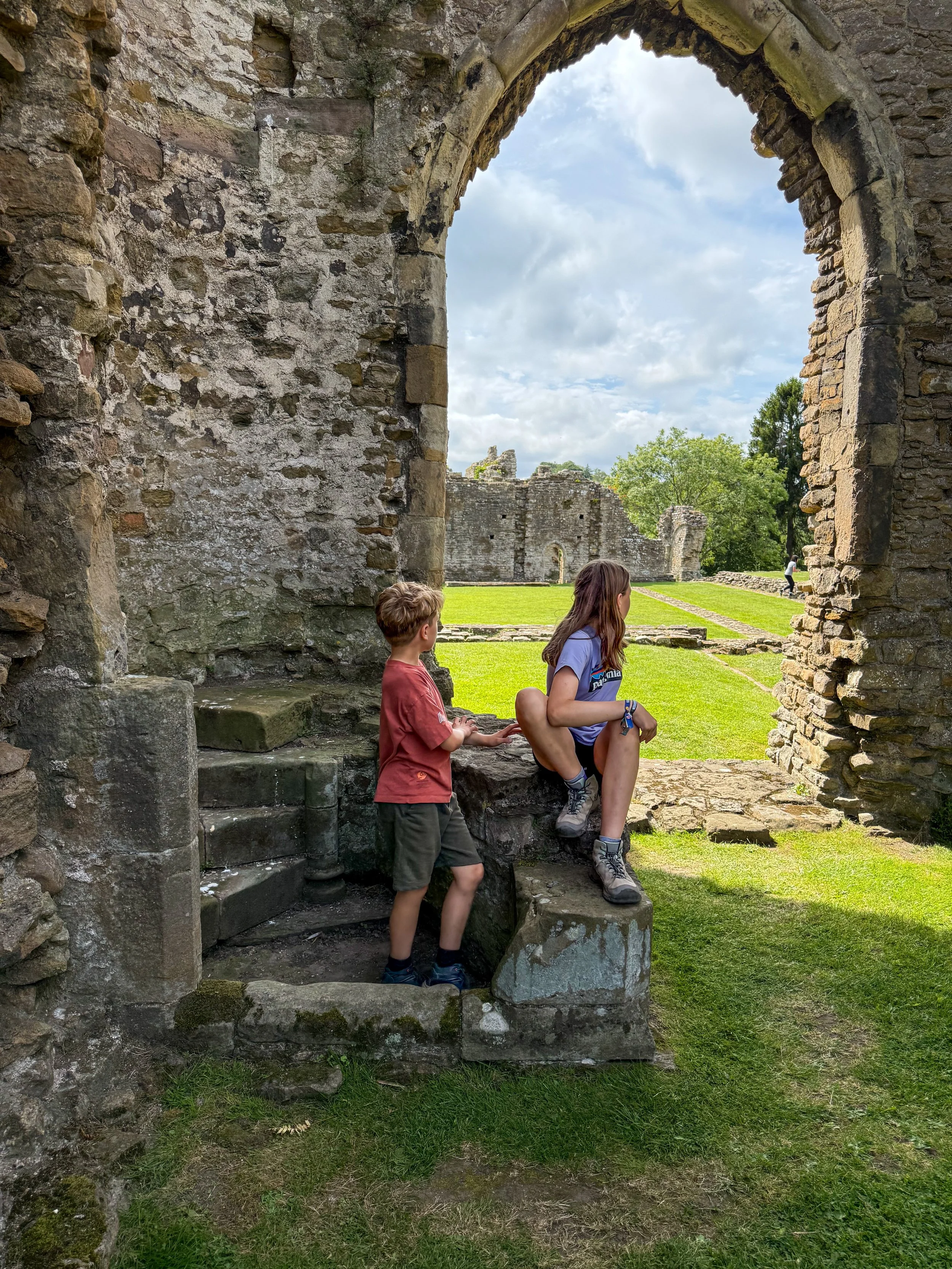 Children looking through a stone archway with abbey ruins behind