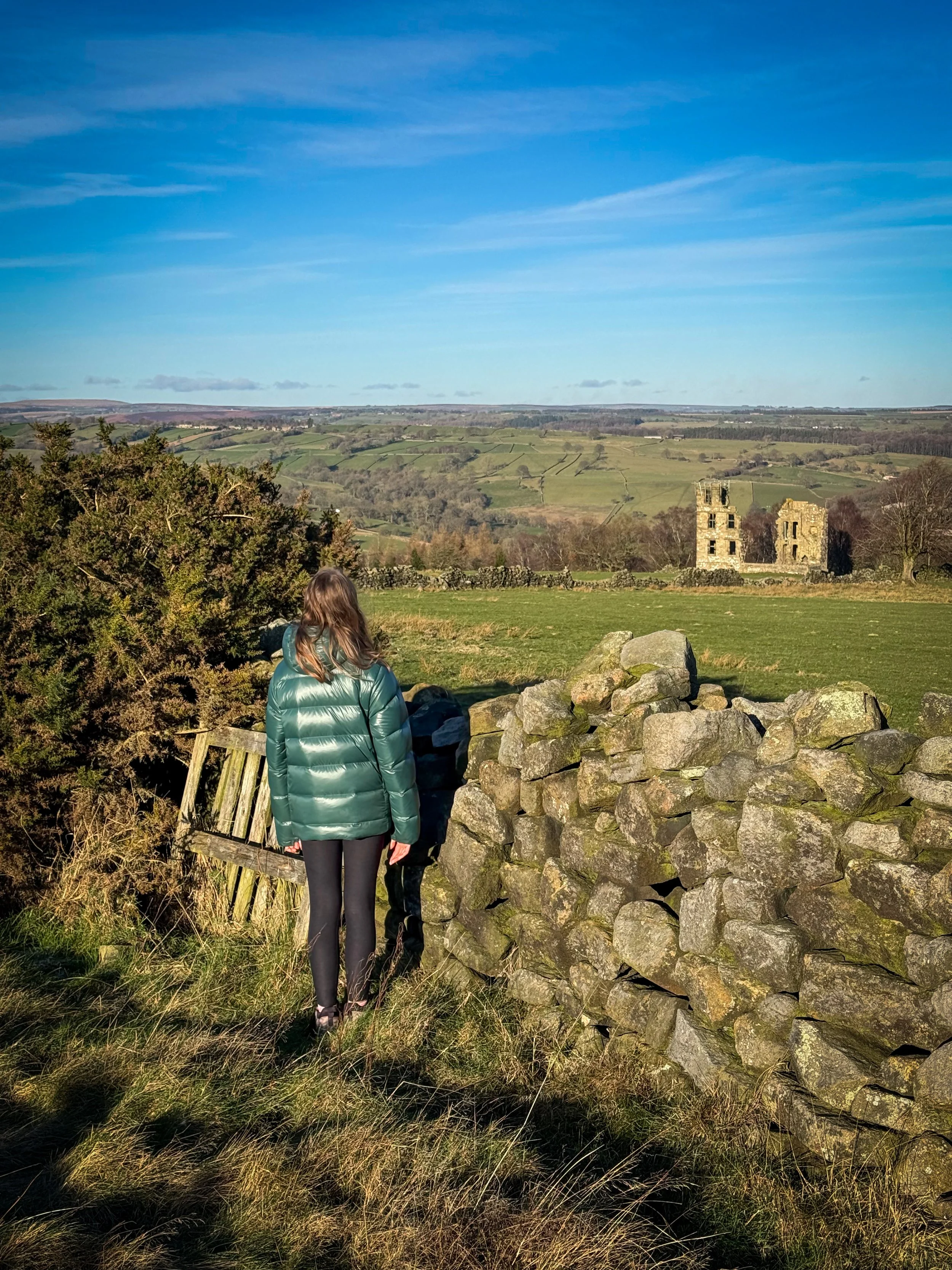 Child looking at the ruins of an old hunting lodge with blue skies and views across moors