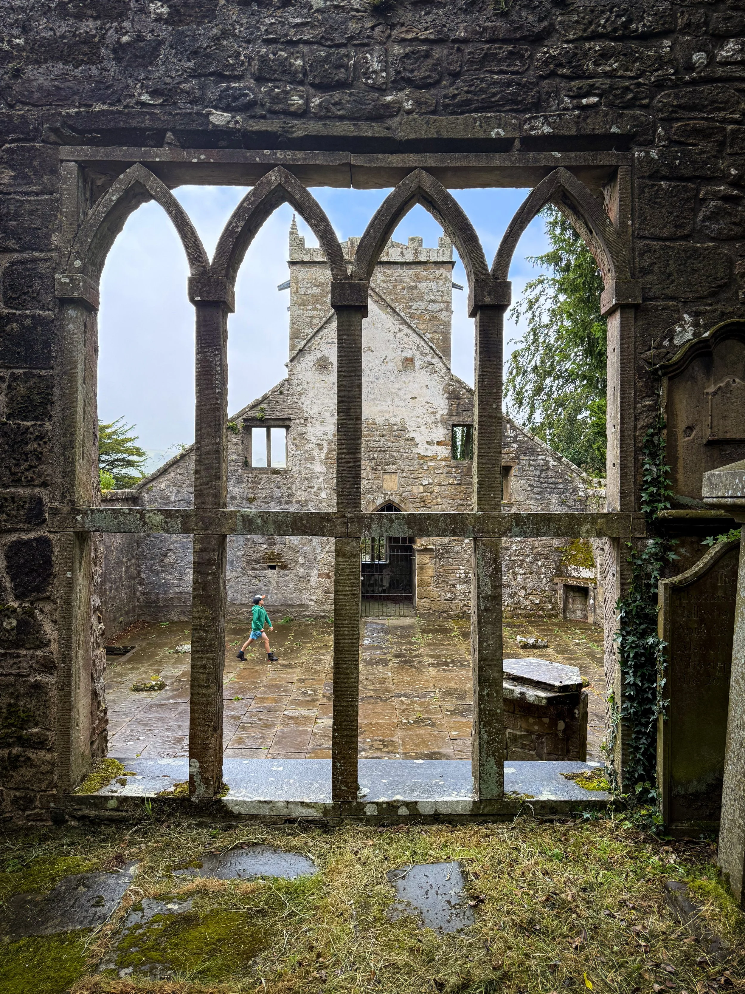 child walking in background through a ruined church with no roof under blue sky with a ruined church window in the foreground