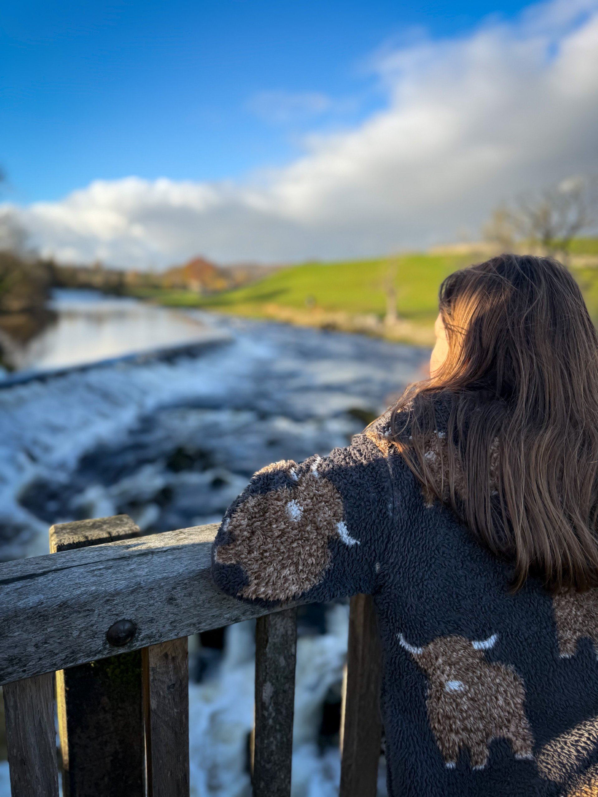 Child standing on the bridge looking at a weir under blue skies