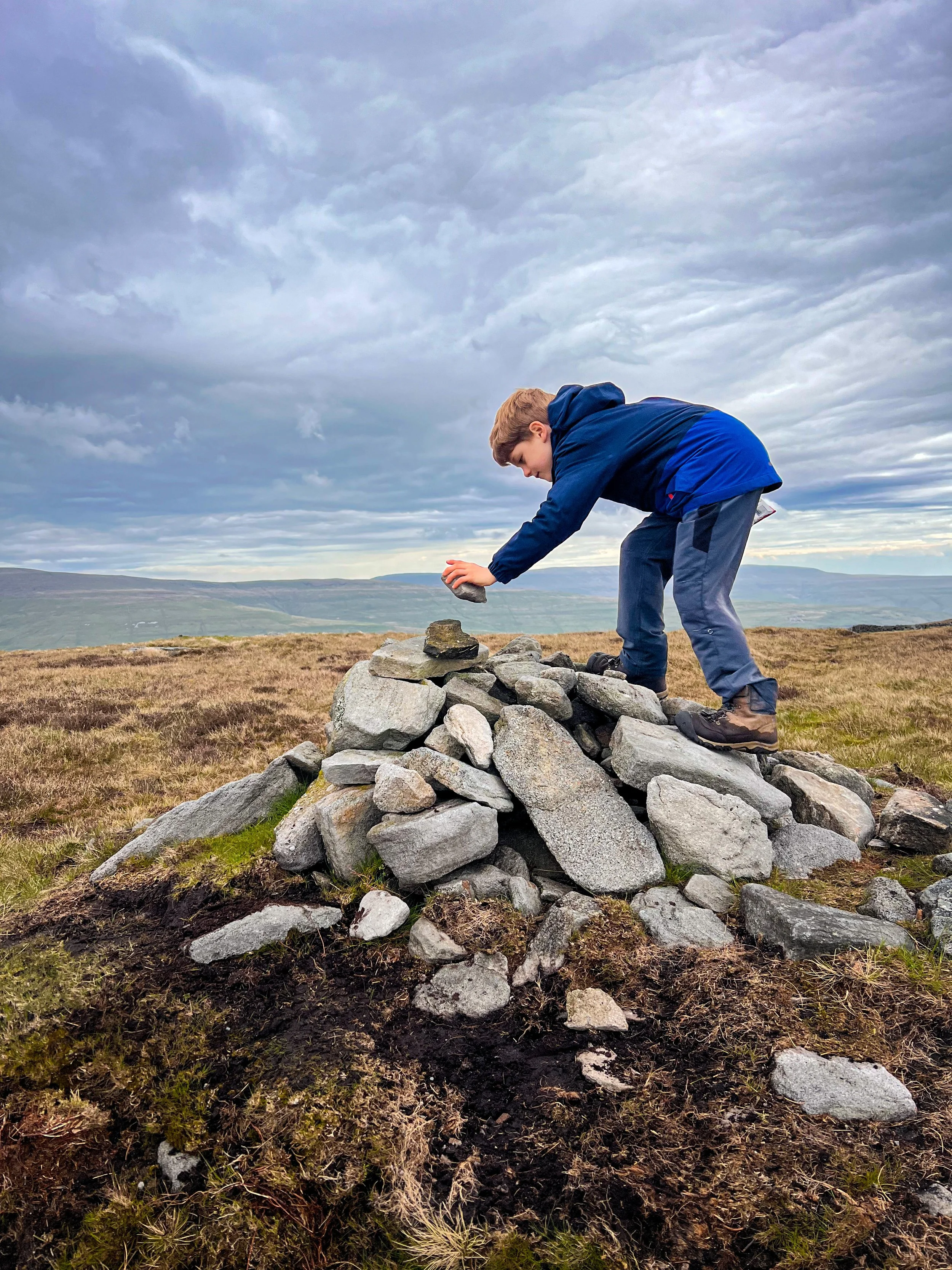Child adding rock to the top of summit cairn