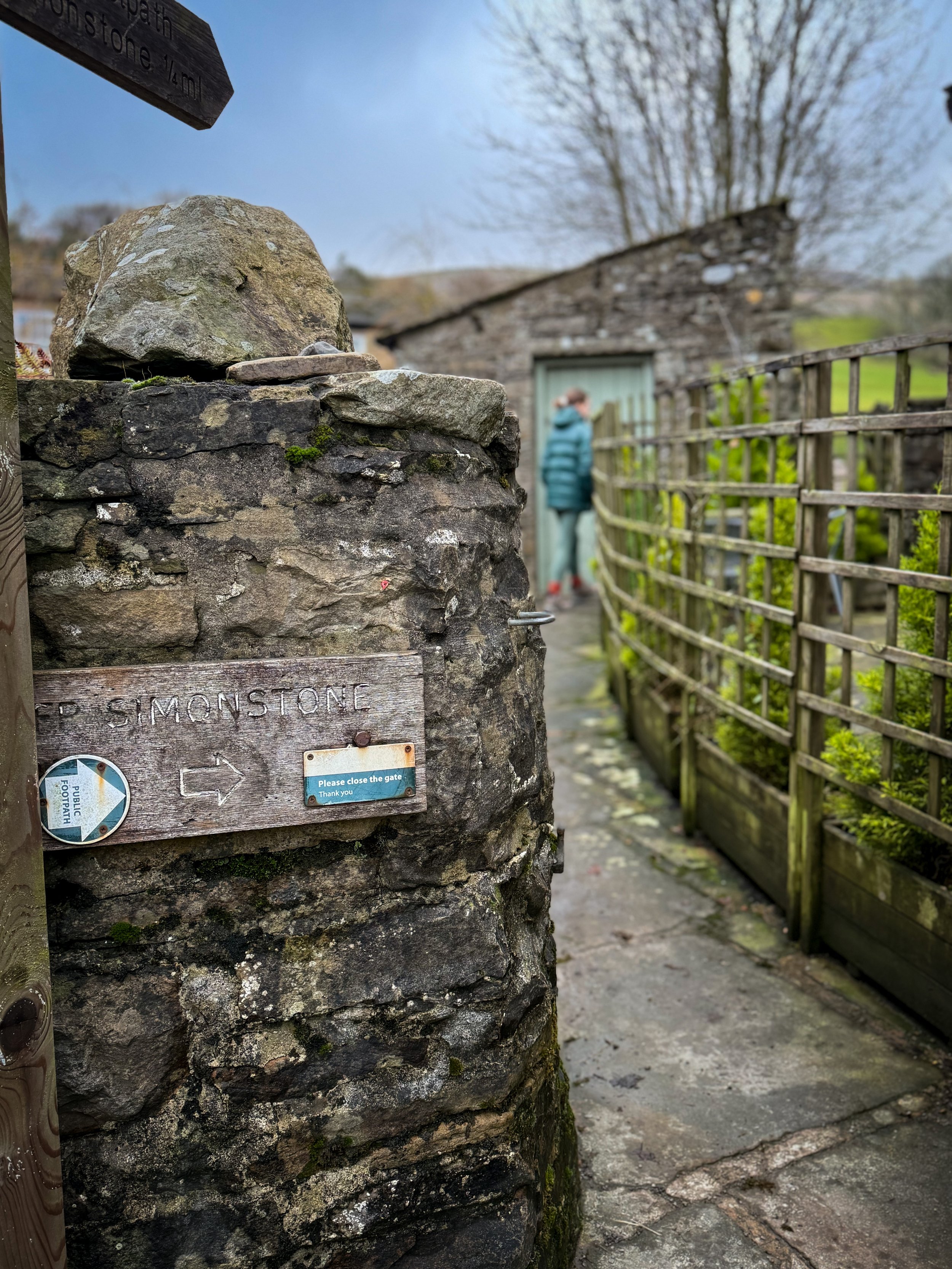 A signpost on a dry stone wall and a child walking down a footpath in the distance