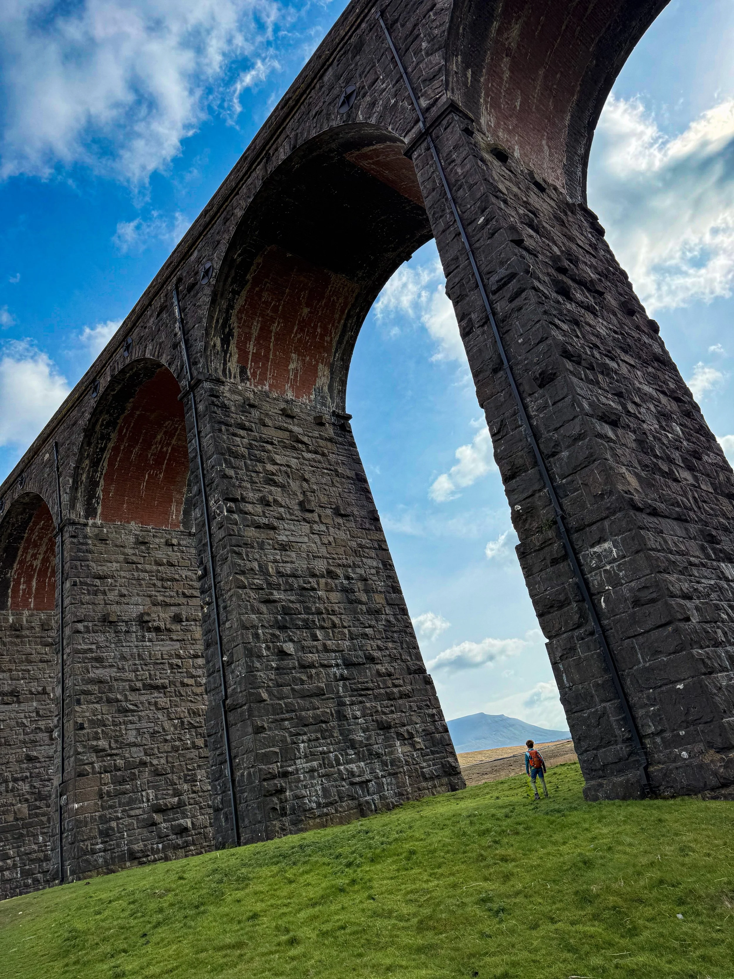 Child standing under massive arches of the Ribblehead viaduct with a view of Ingleborough moutain behind