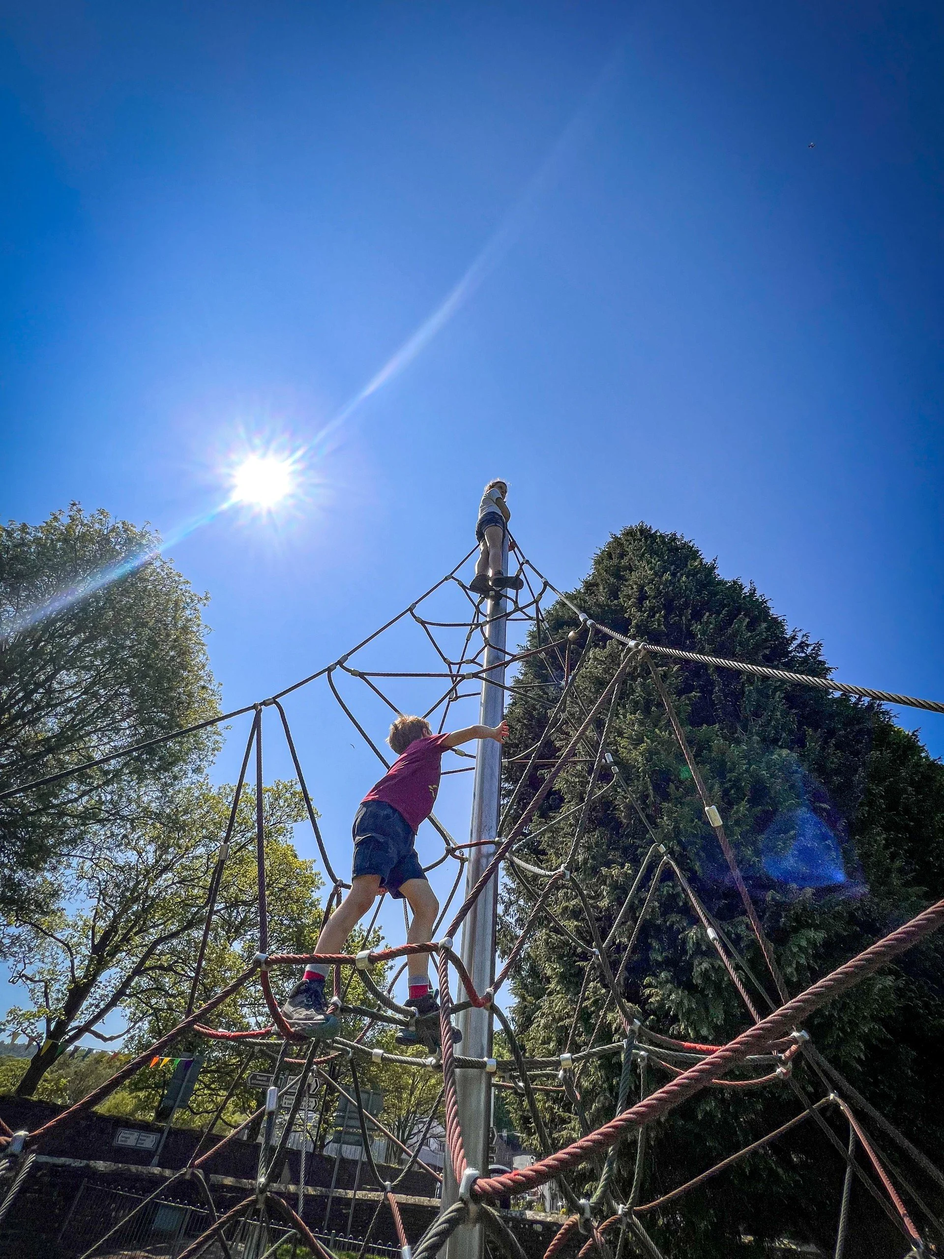 Two children climbing a triangular climbing frame under blue skies and sun