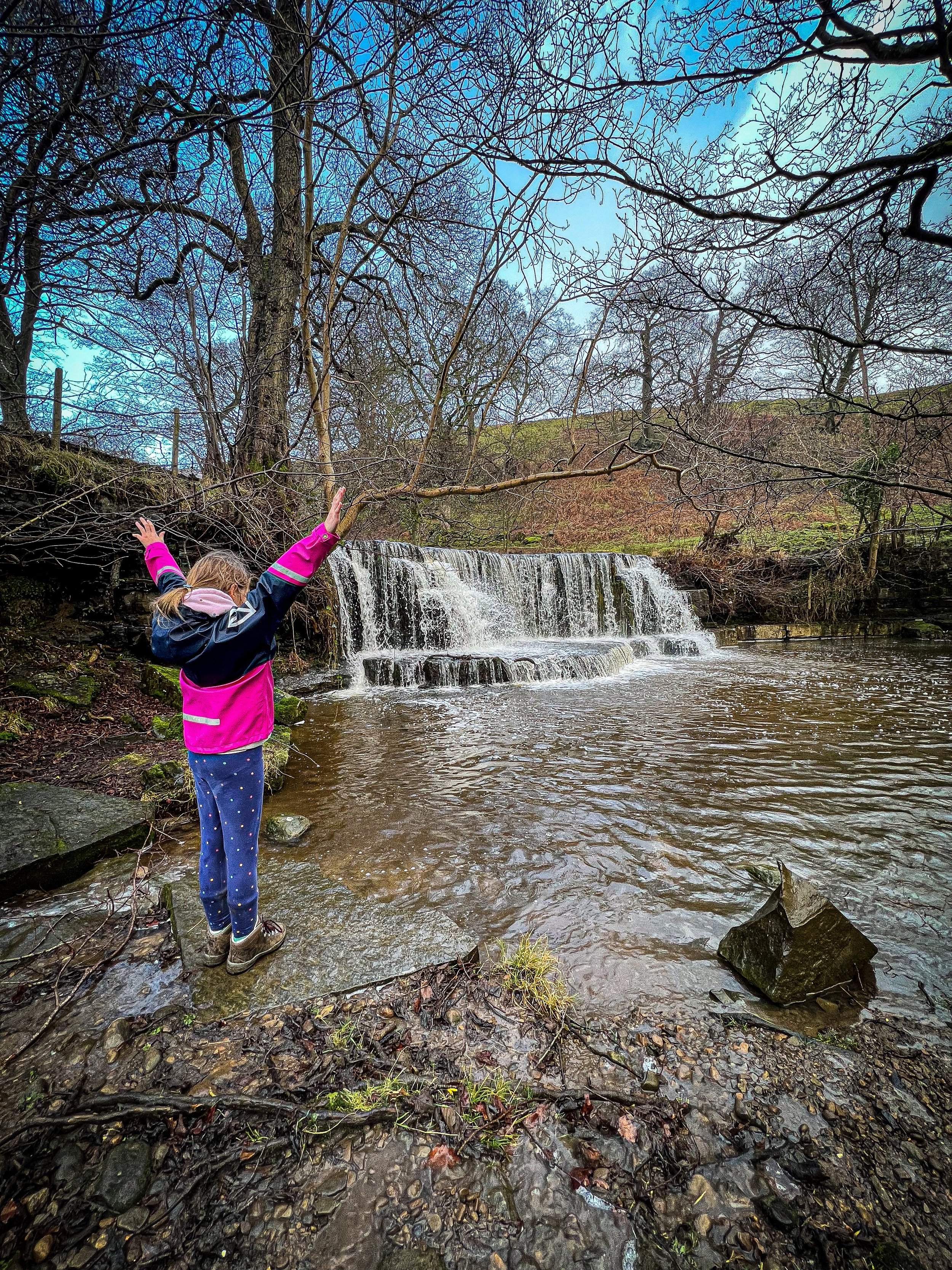 Child standing with arms in the air with waterfall in background in winter