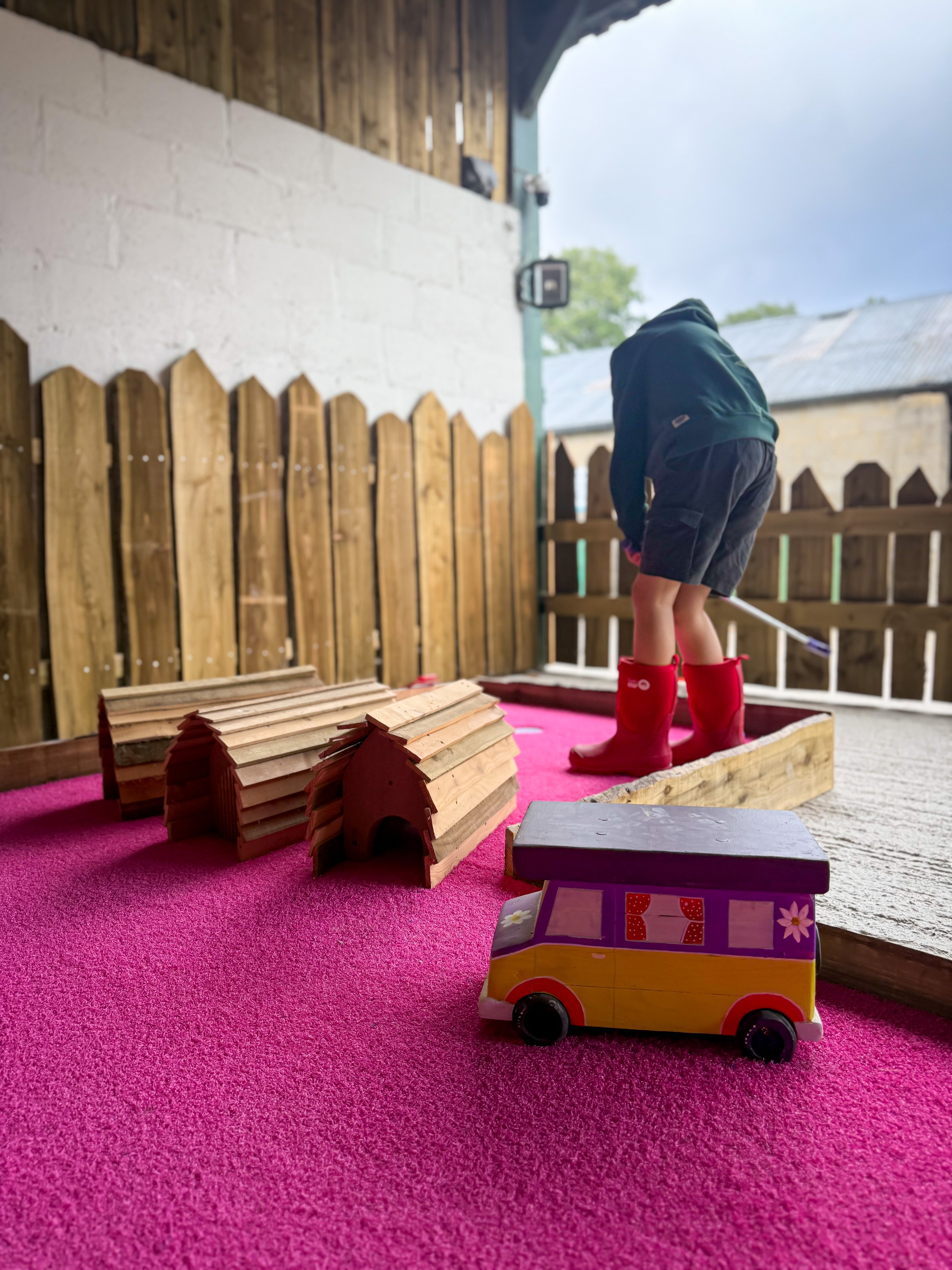 child playing crazy golf surrounded by wooden fence and with a pink felt design
