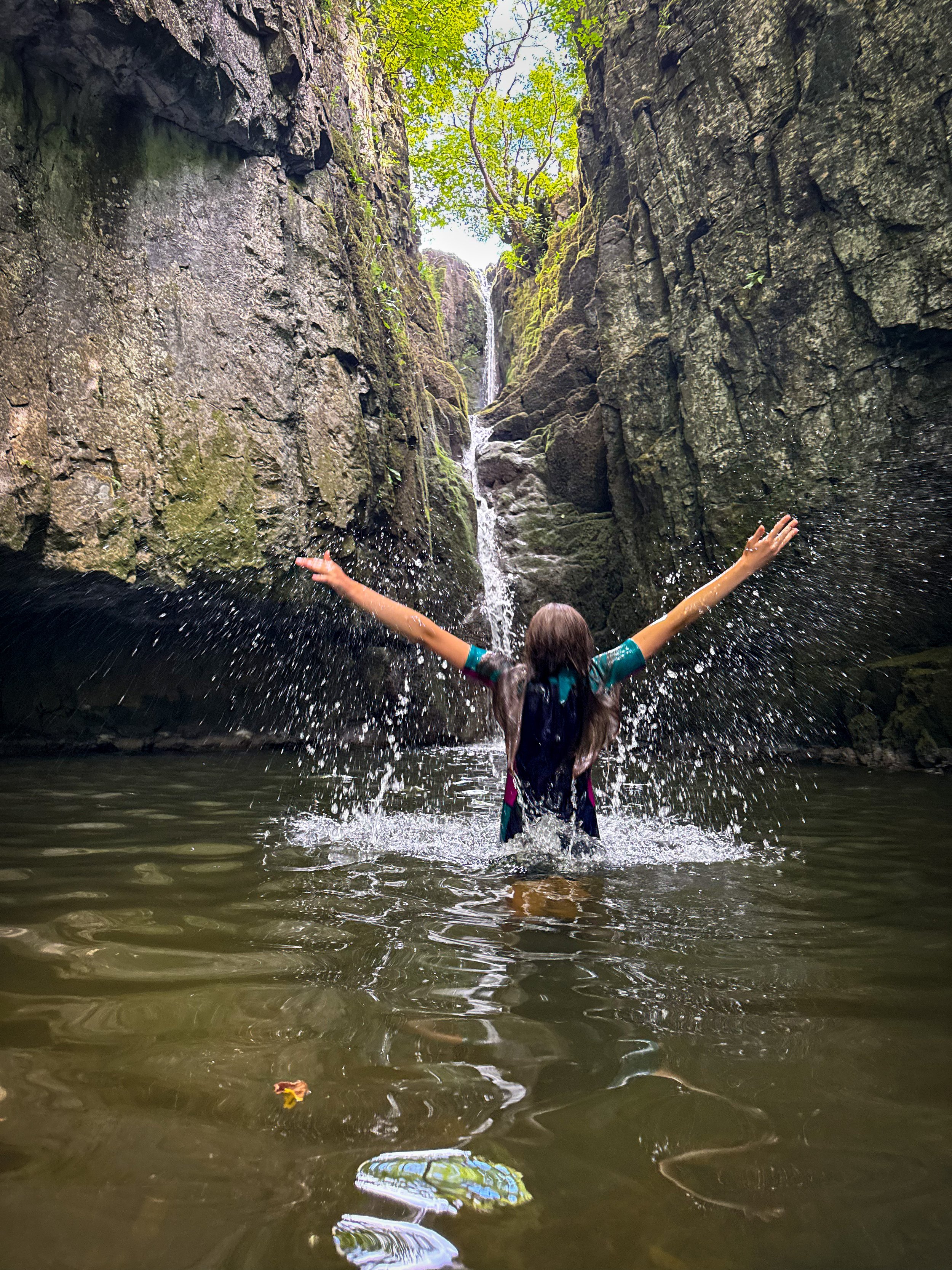 Child jumping in the air at a waterfall whilst swimming in the water with water splashing