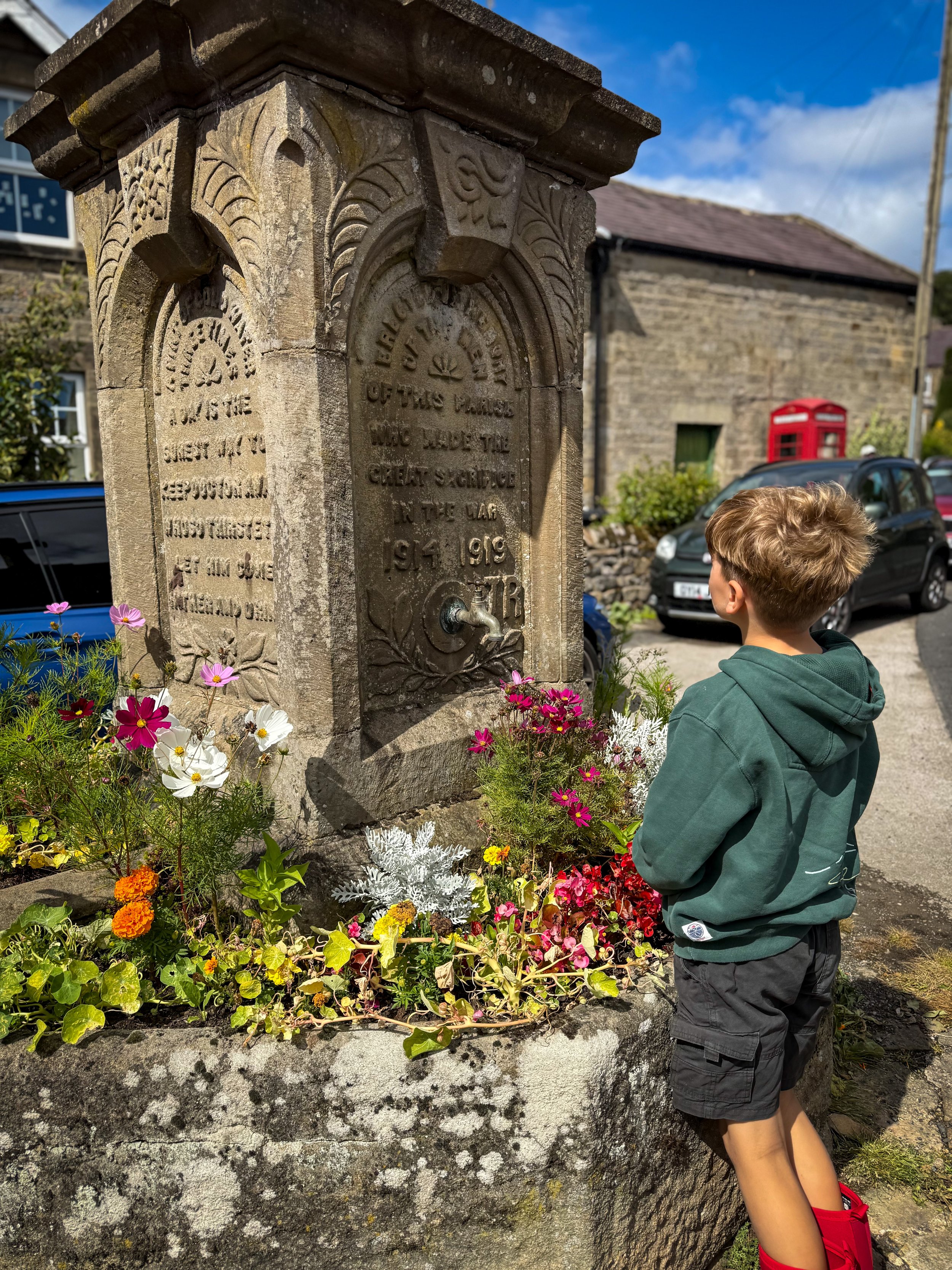 Child standing reading a stone war memorial surrounded by flowers
