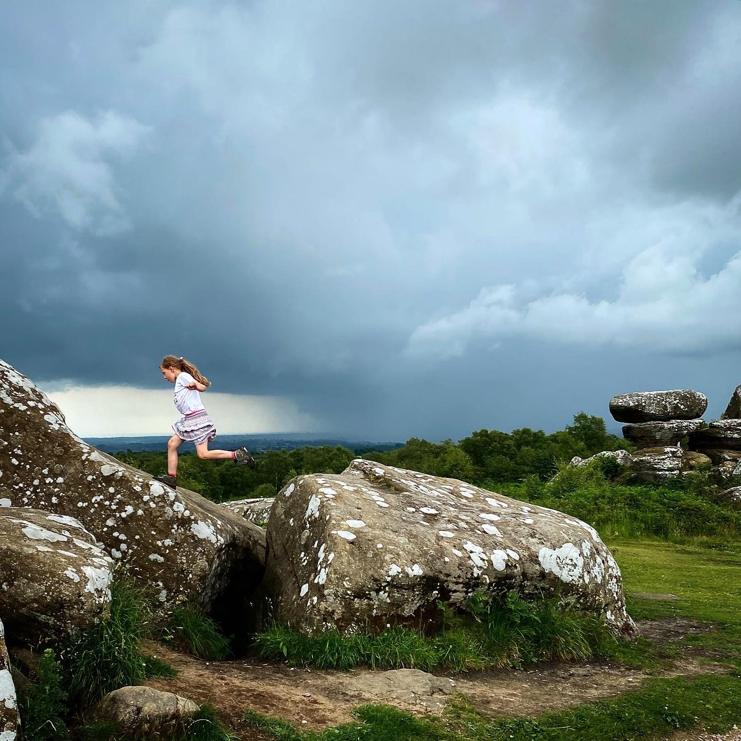 Child running across Brimham rock formation with stormy skies