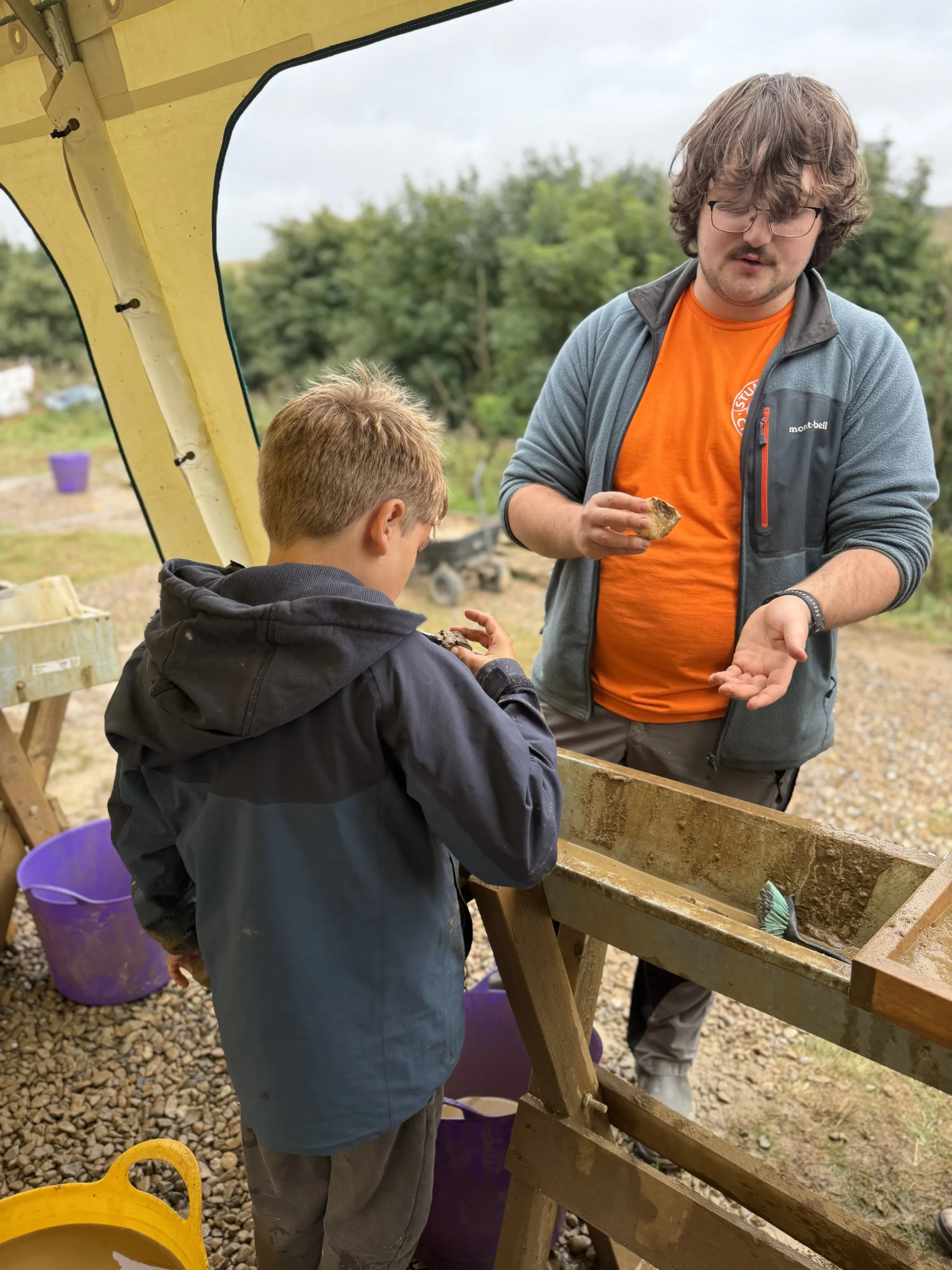 Child talking to a guy in an orange tshirt about rocks surrounded by dig materials