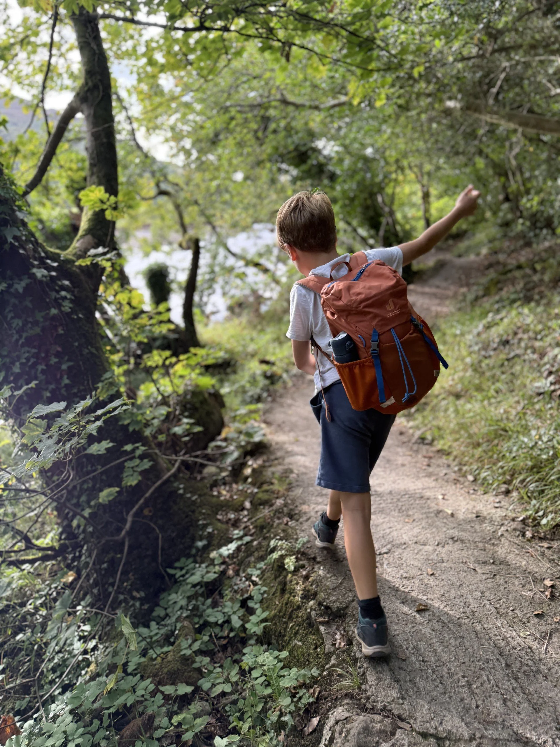 Child with arms swinging walking along a riverside path with trees each side