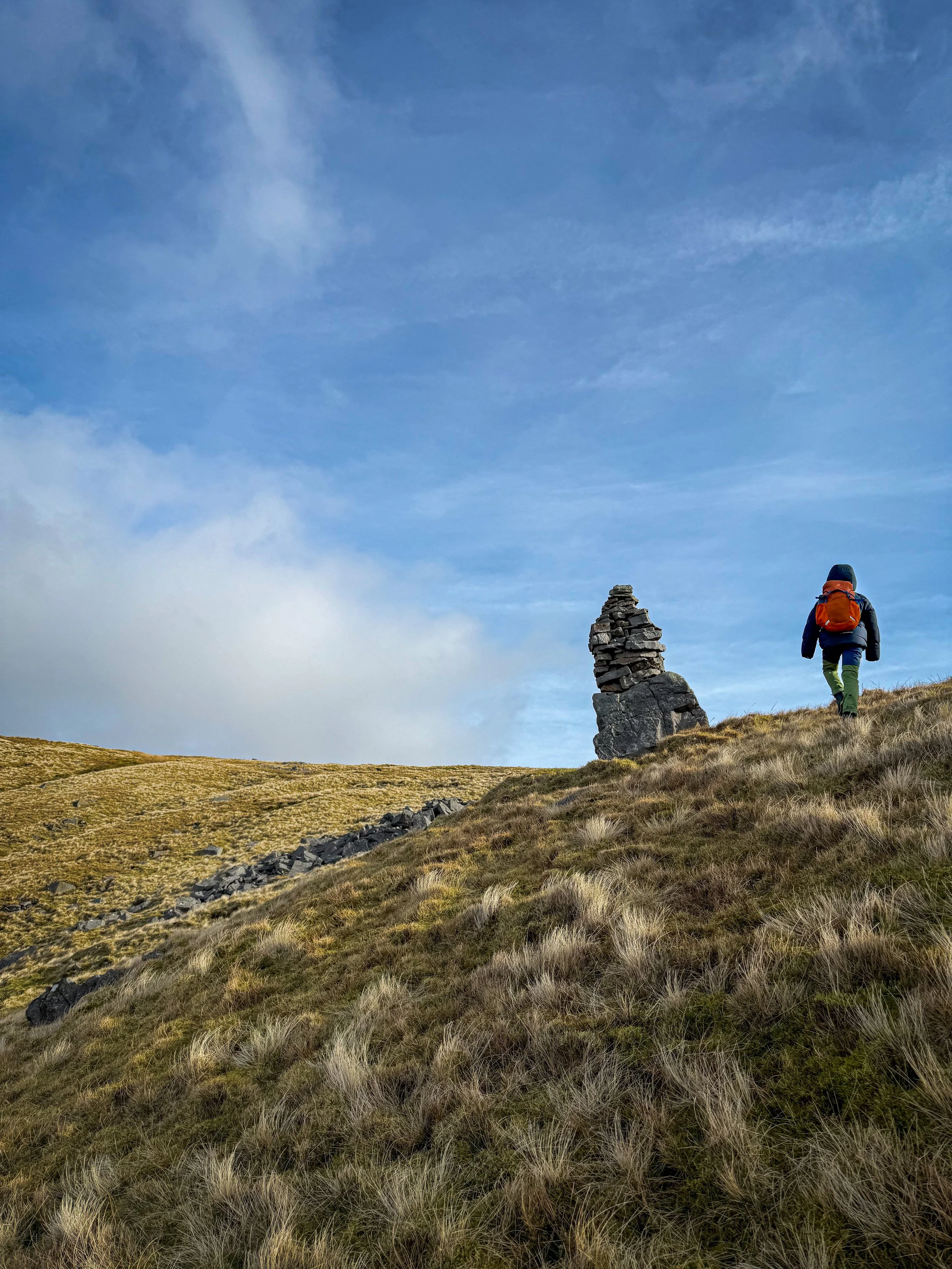 Child walking towards a cairn on the side of a hill with blue skies above