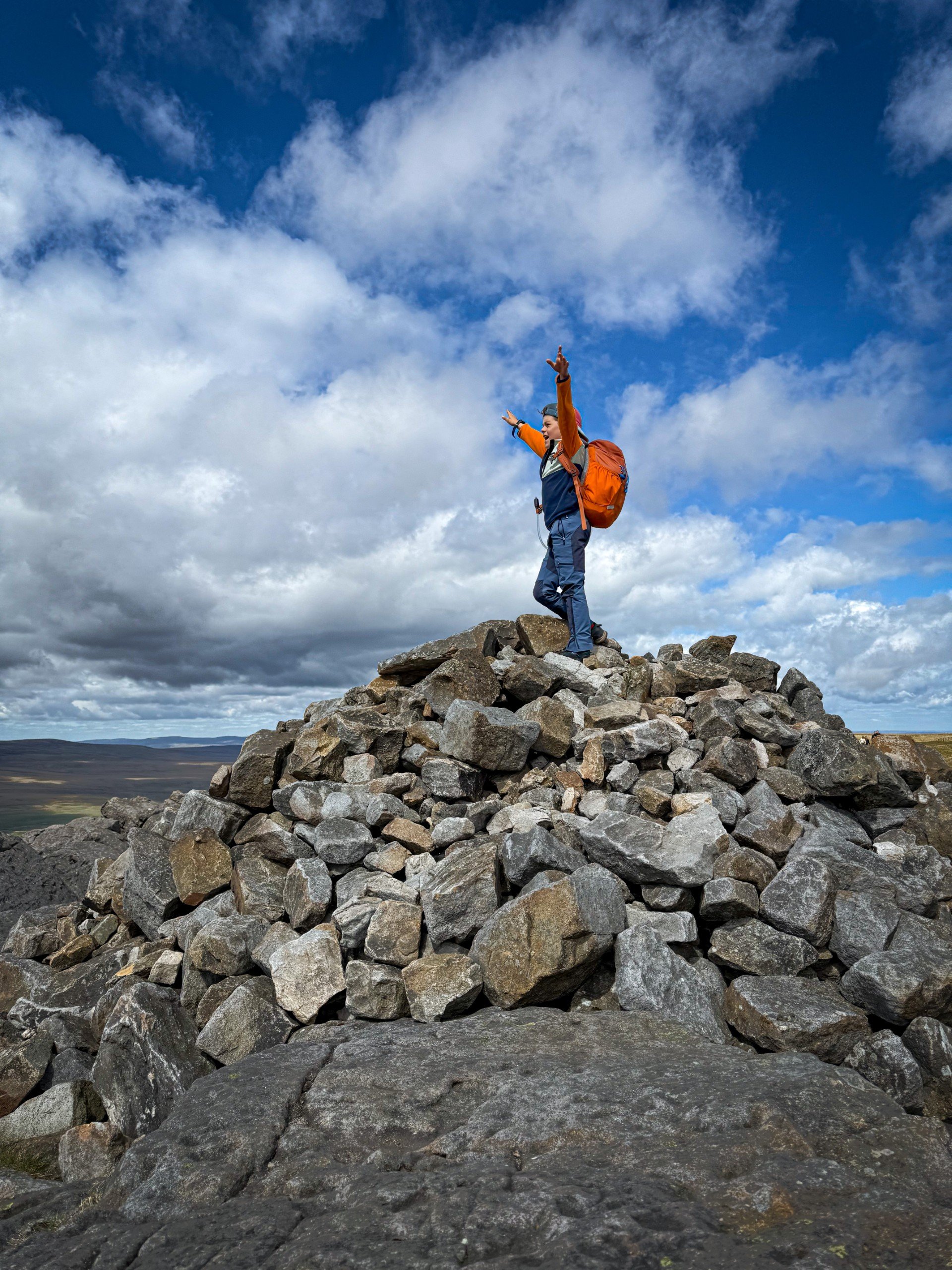 Child with his hands in the air on top of a cairn under blue skies