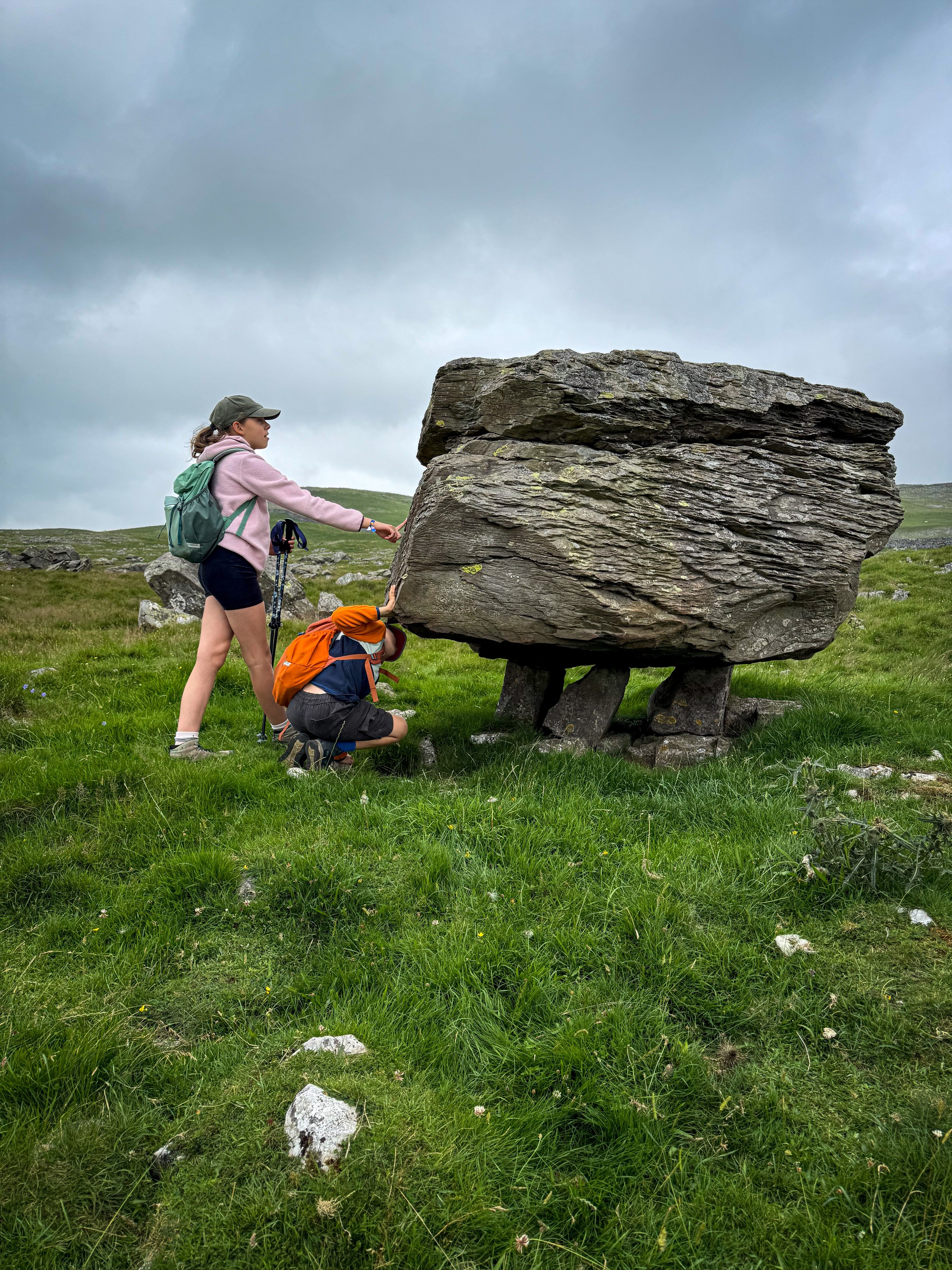 Two children looking at a large rock balanced on three small rock