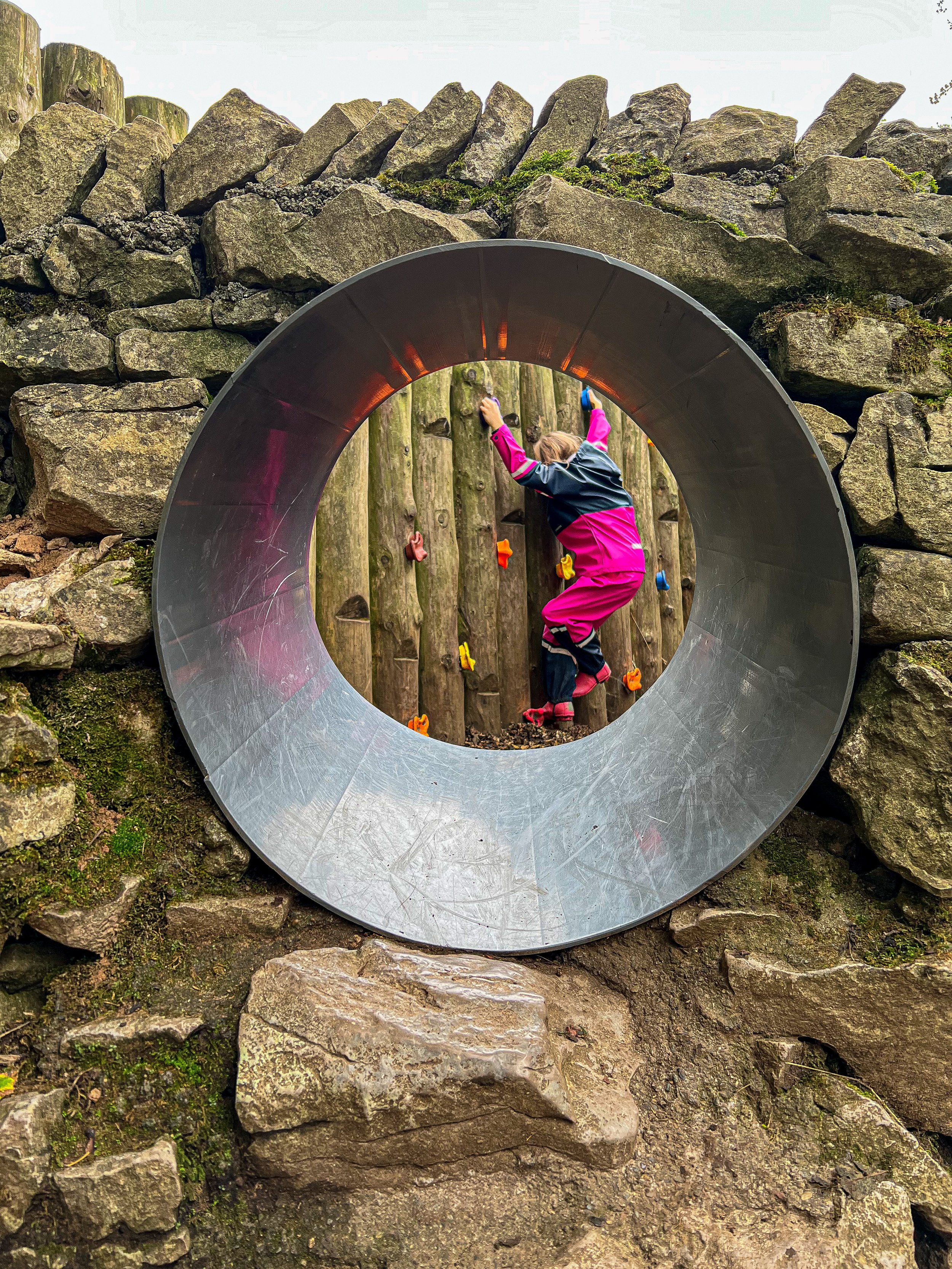 child climbing up the climbing wall in distance shot through a tunnel