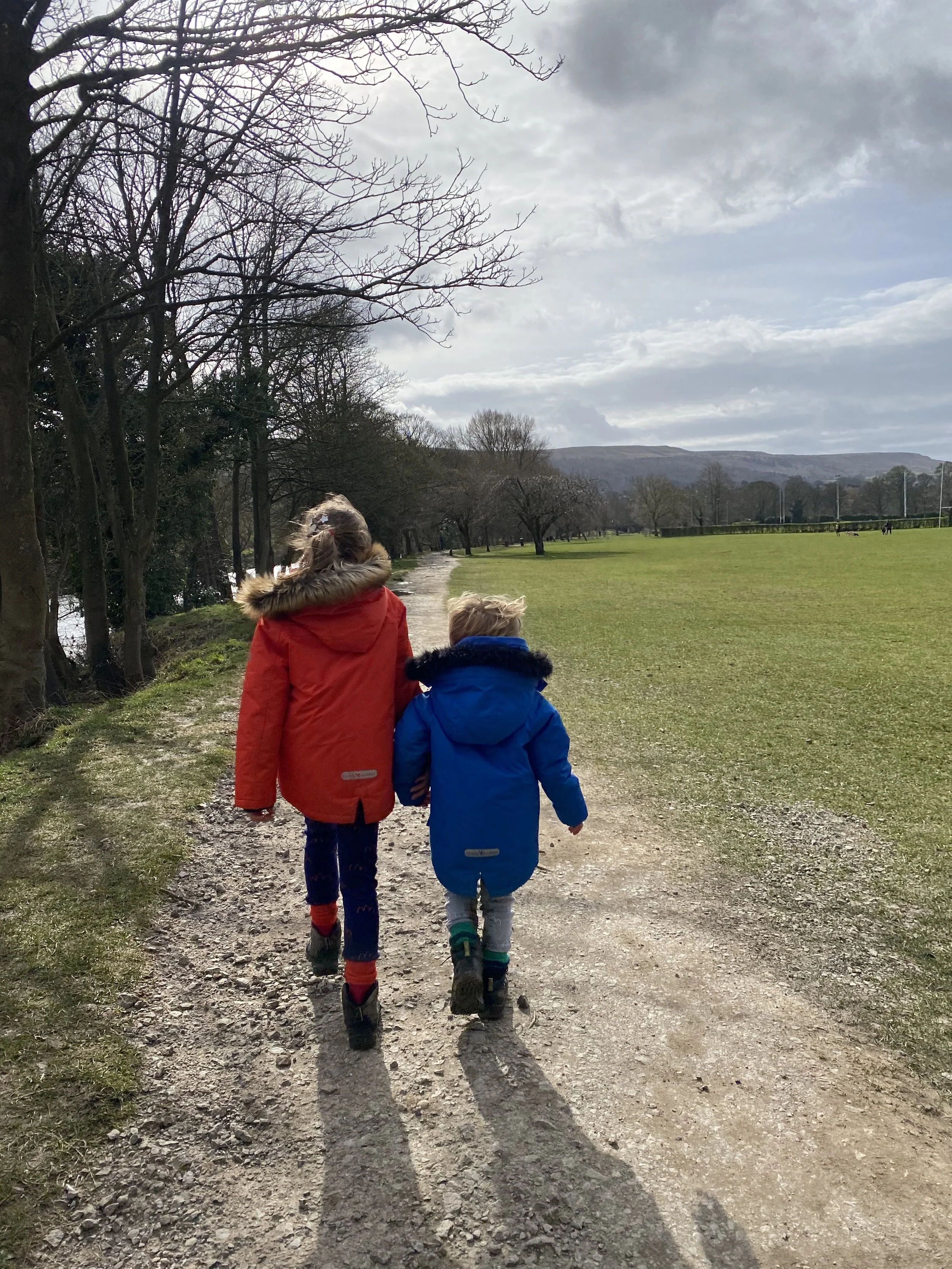 Two children walking along a wide path in winter with fields to the right