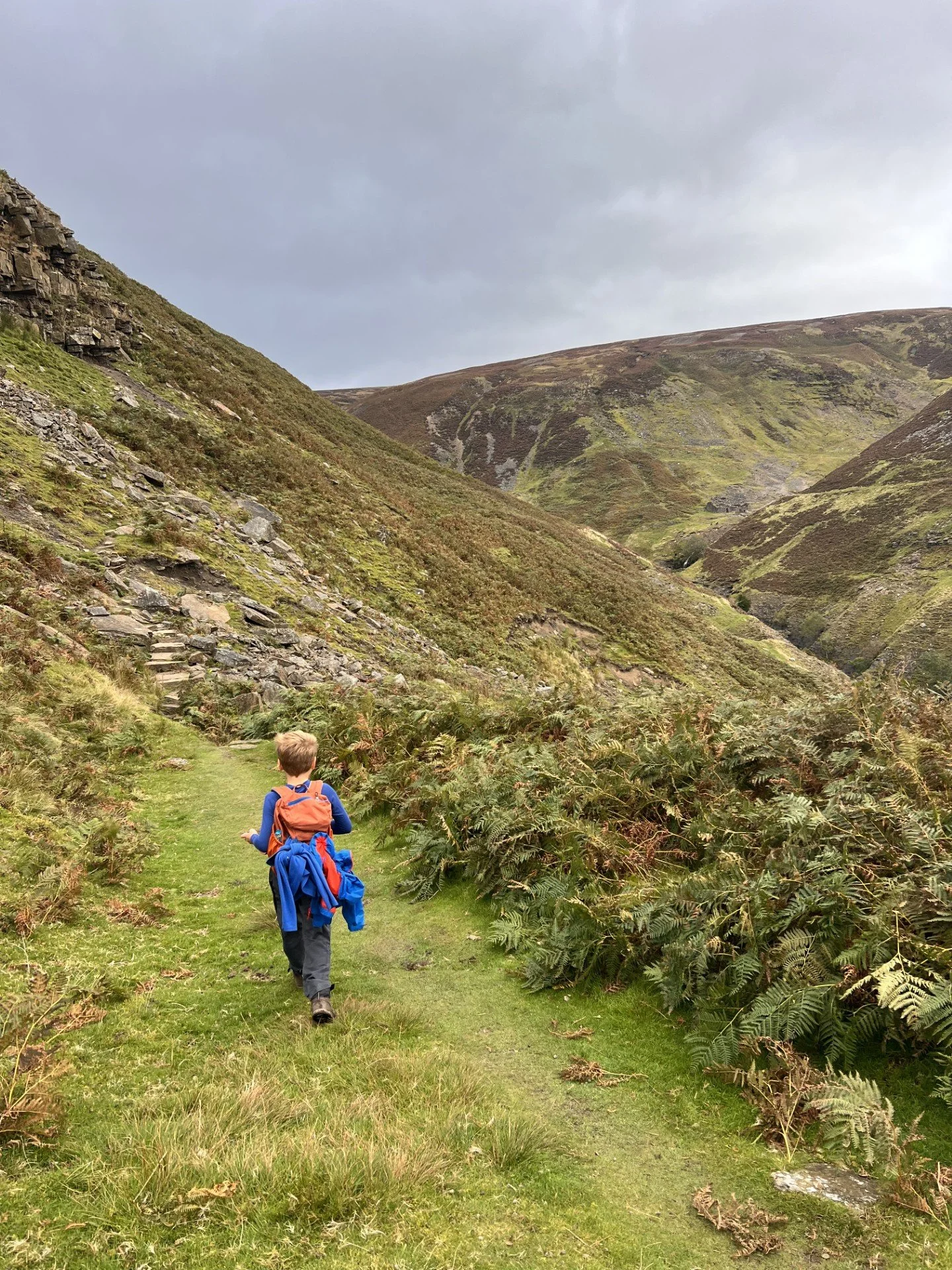 Child walking along path in a steep sided valley with rocks tumbling down hillside
