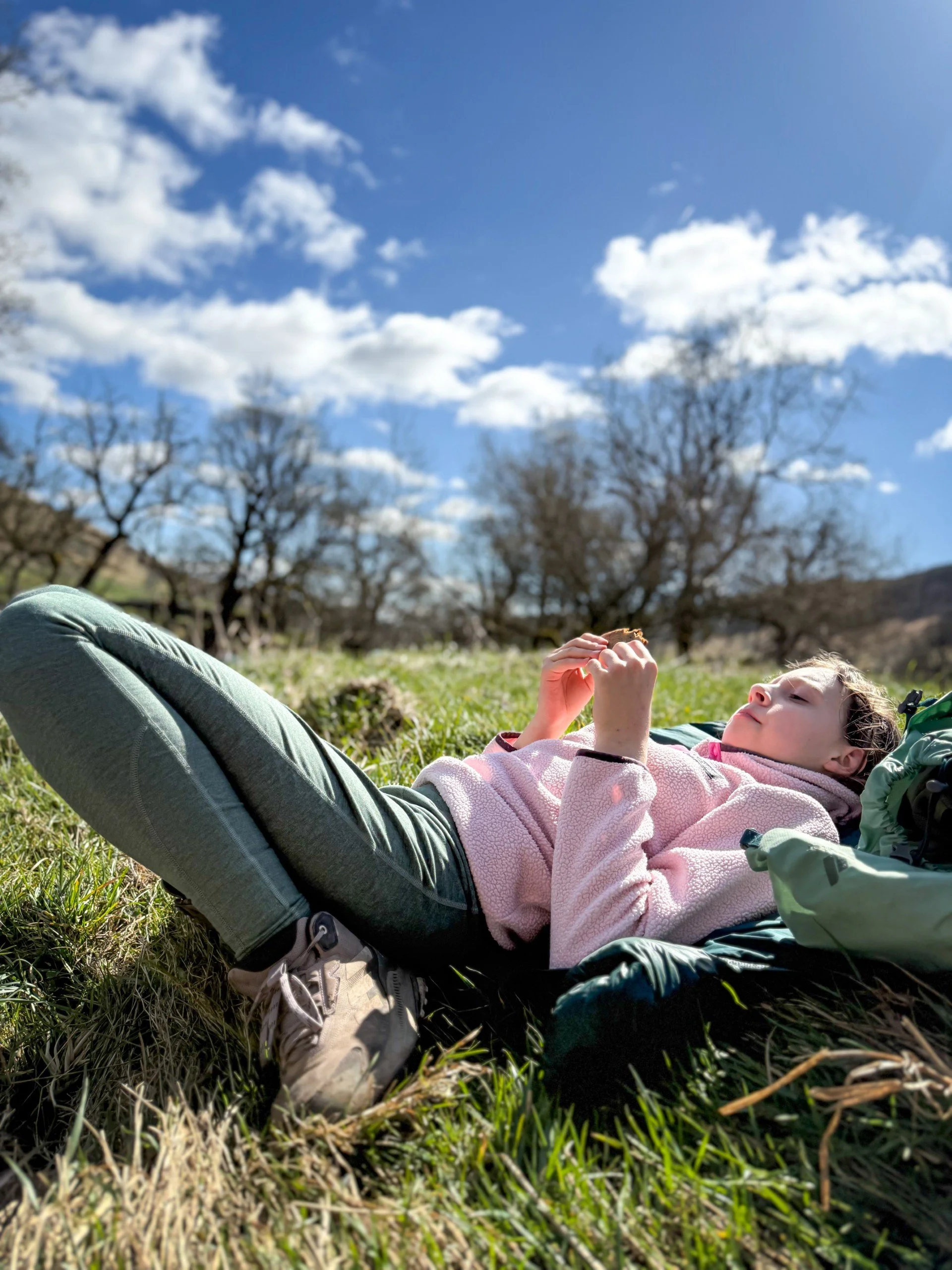 Child lying down eating a cookie under blue skies on the grass