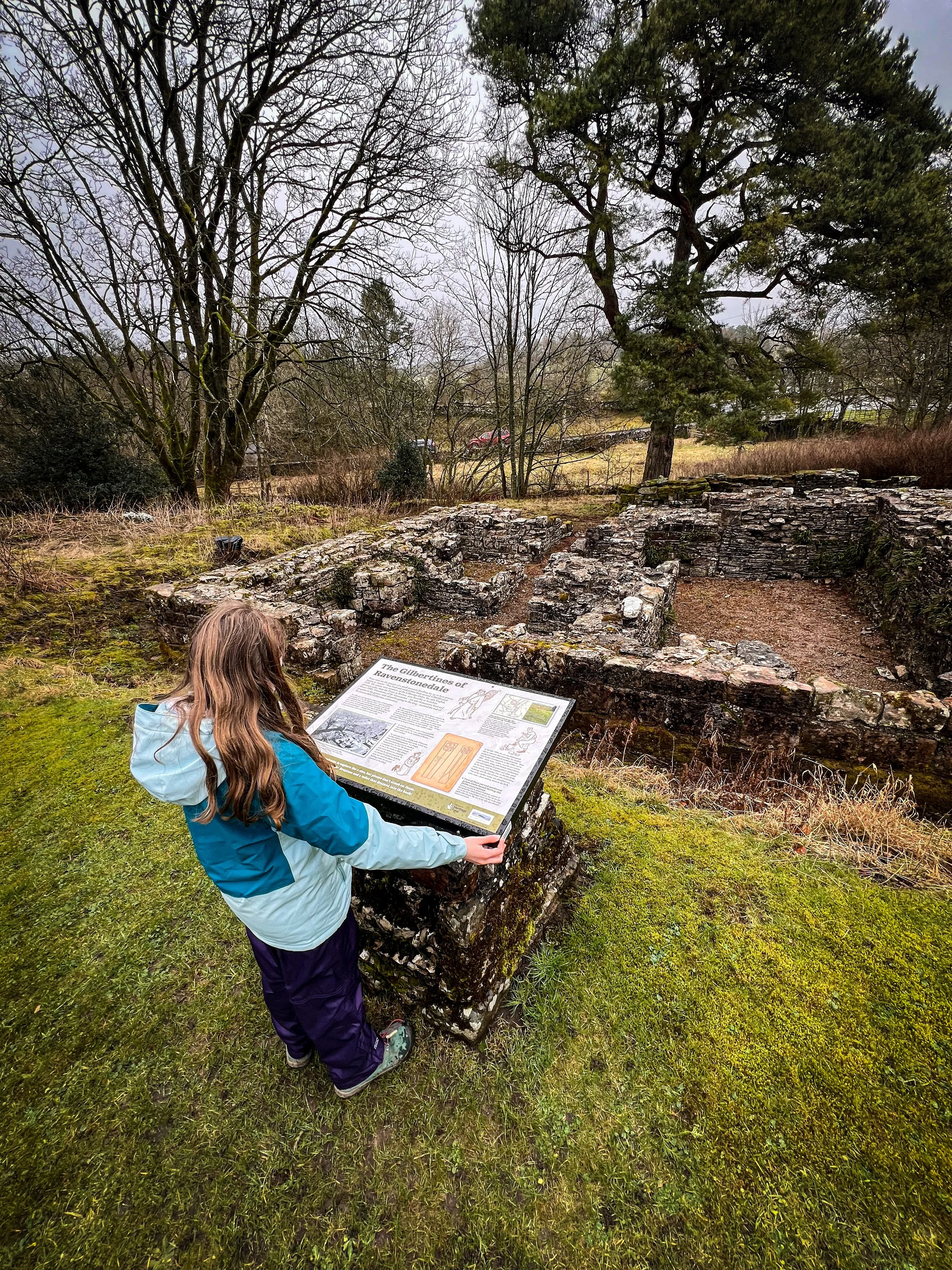 Child standing at an information board in front of a ruined abbey