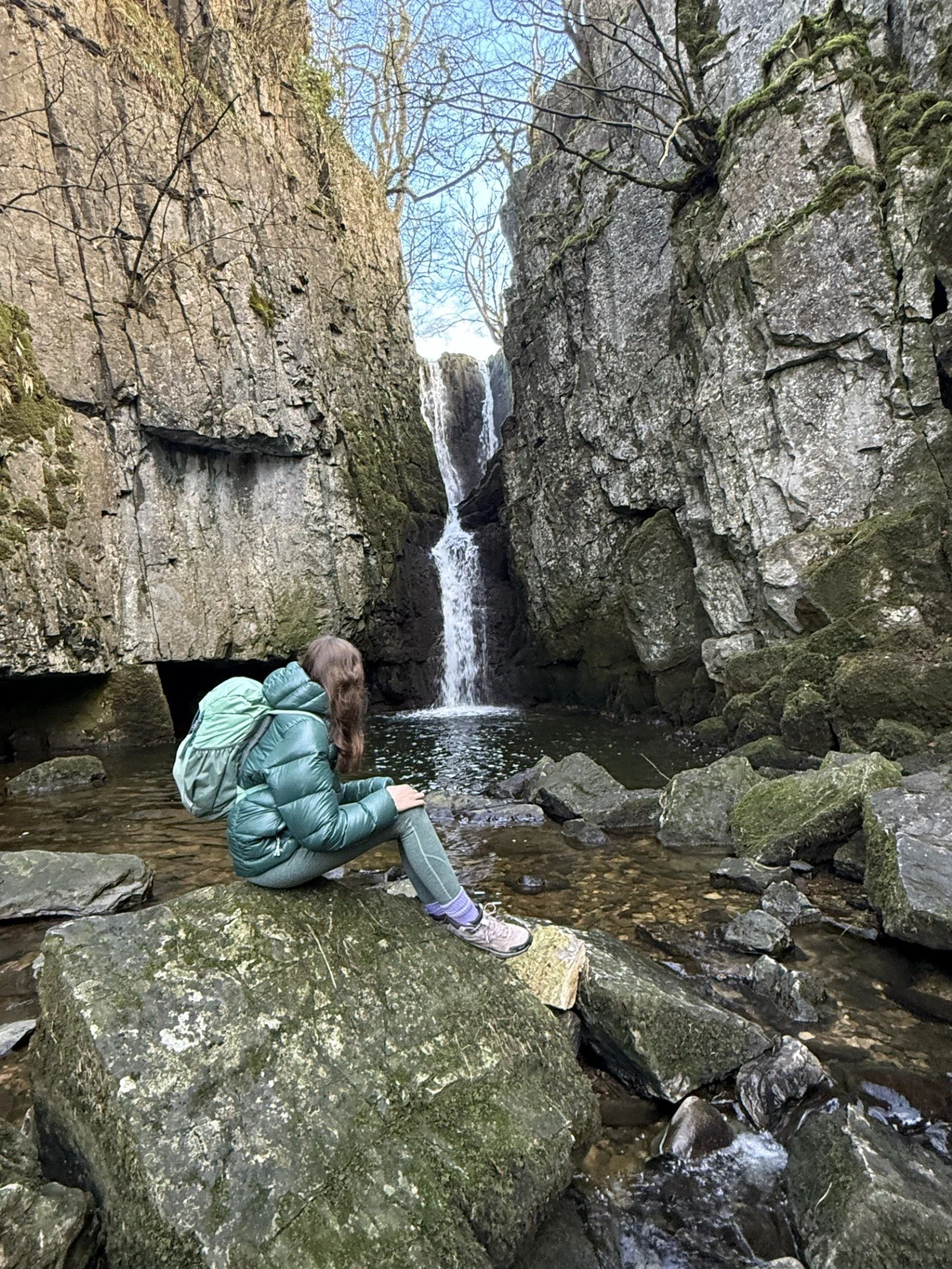 Child sitting in front of Catrigg Force waterfall with rocky sides in winter