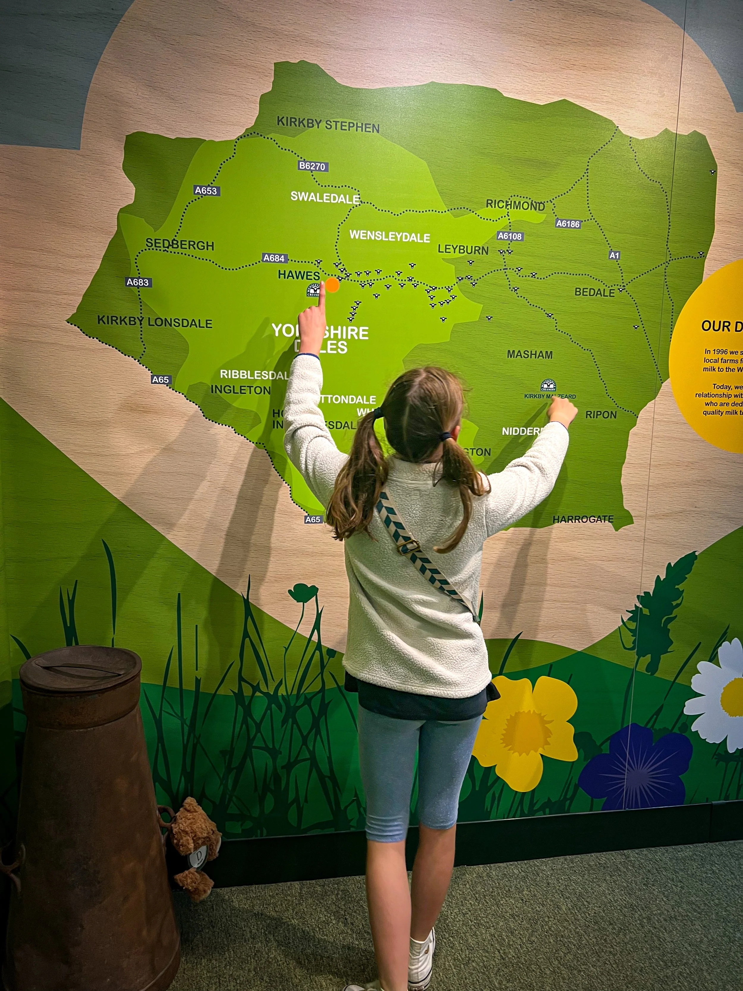 A child in a white top and bunches pointing at a green map of the Yorkshire Dales