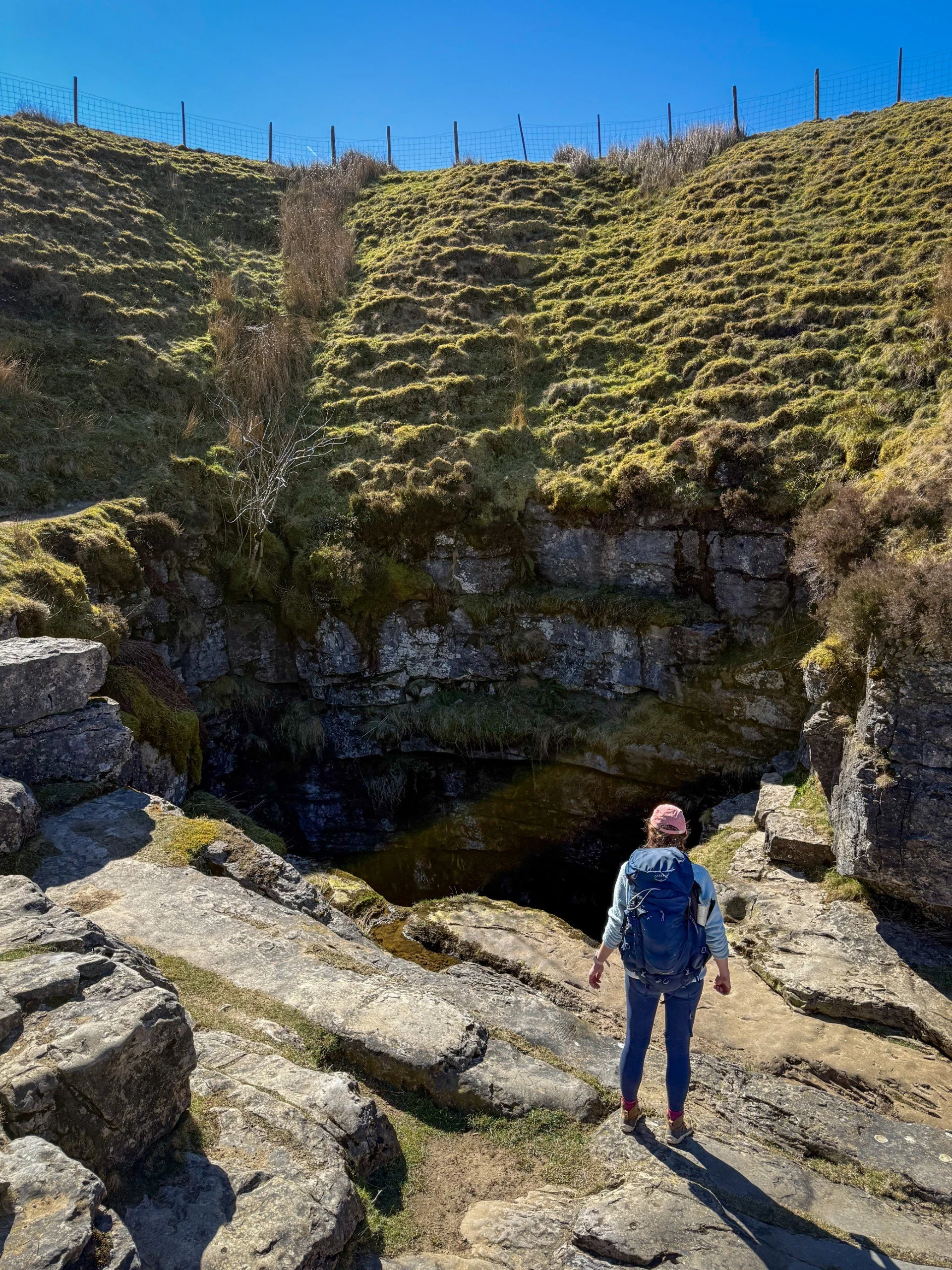 woman standing in front of large shadowy hole in rocky surroundings