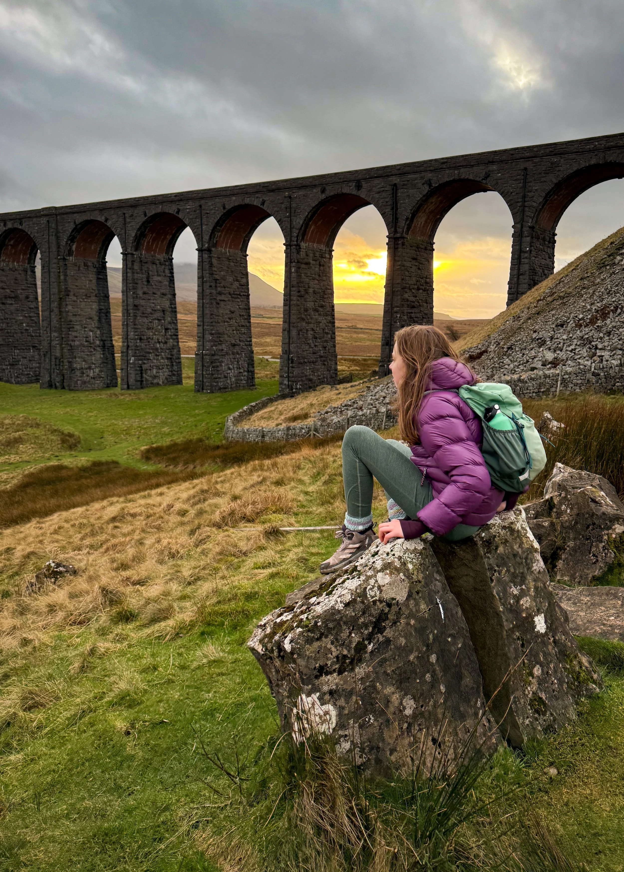 A child sitting in front of the Ribblehead viaduct arches in low winter sun