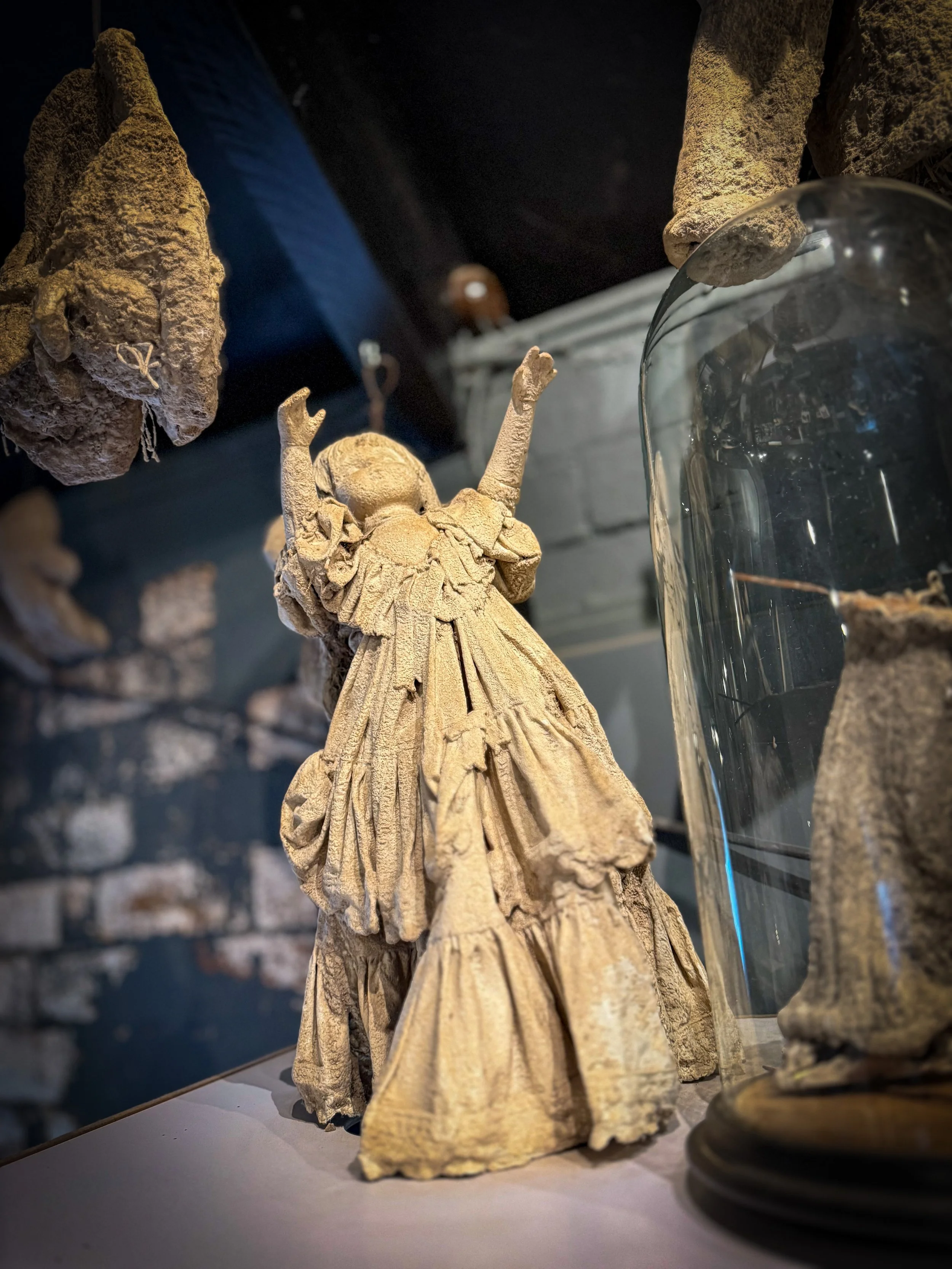 a petrified doll with arms upstretched in a museum